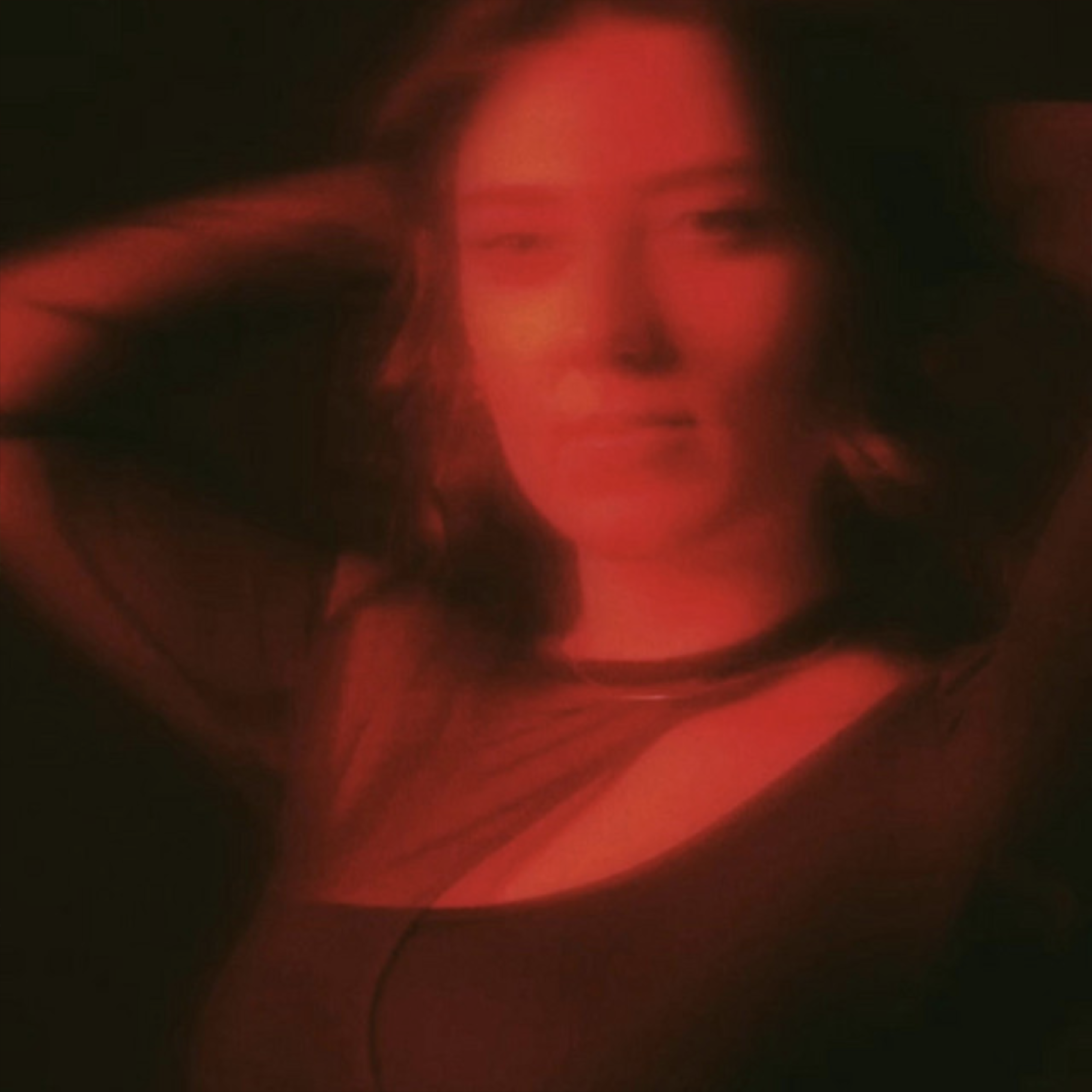 Woman with relaxed expression posing under red lighting in a dark setting.