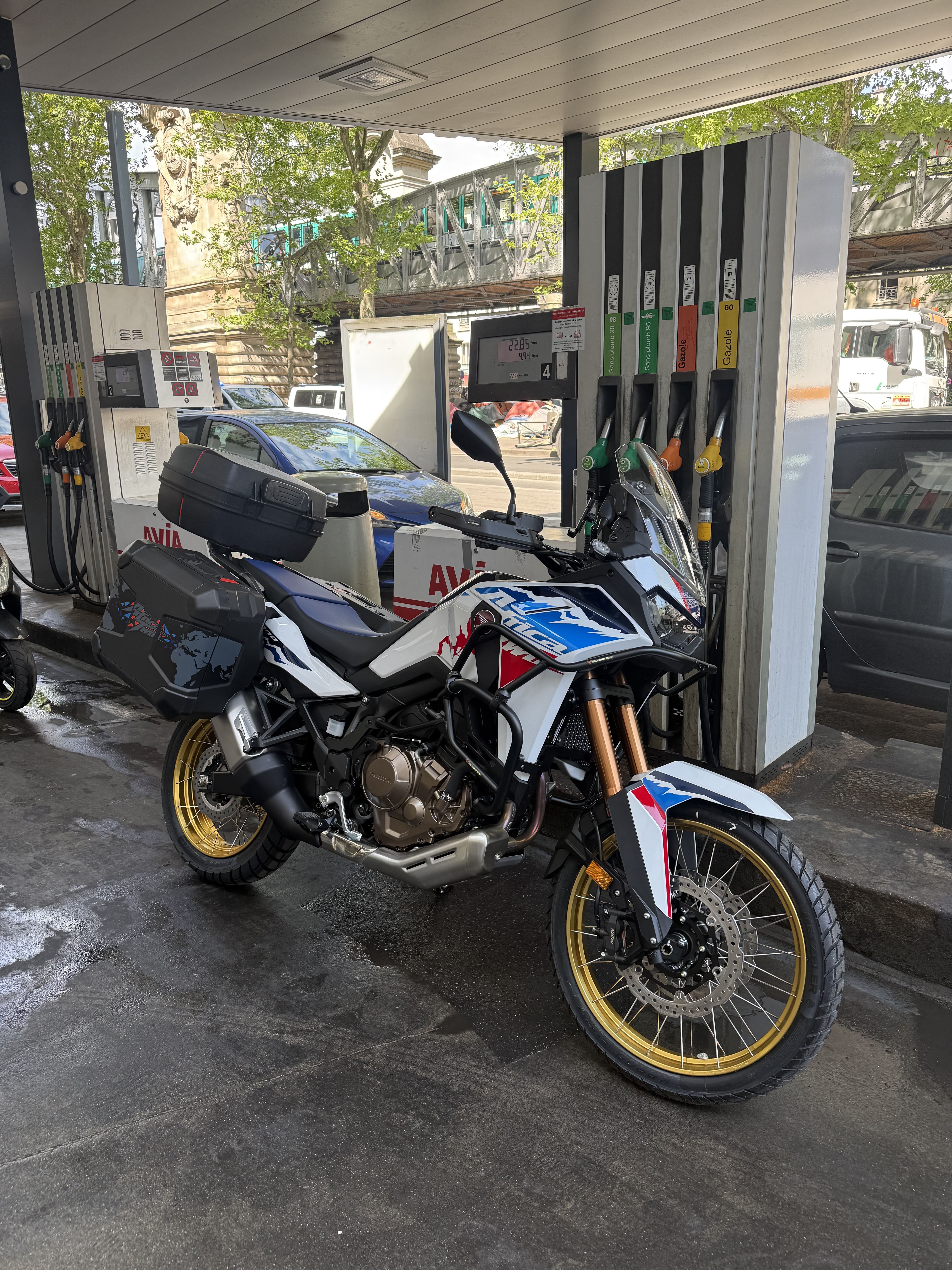 Honda Africa Twin chargée d'un top-case et de sacoches, arrêtée à une pompe à essence