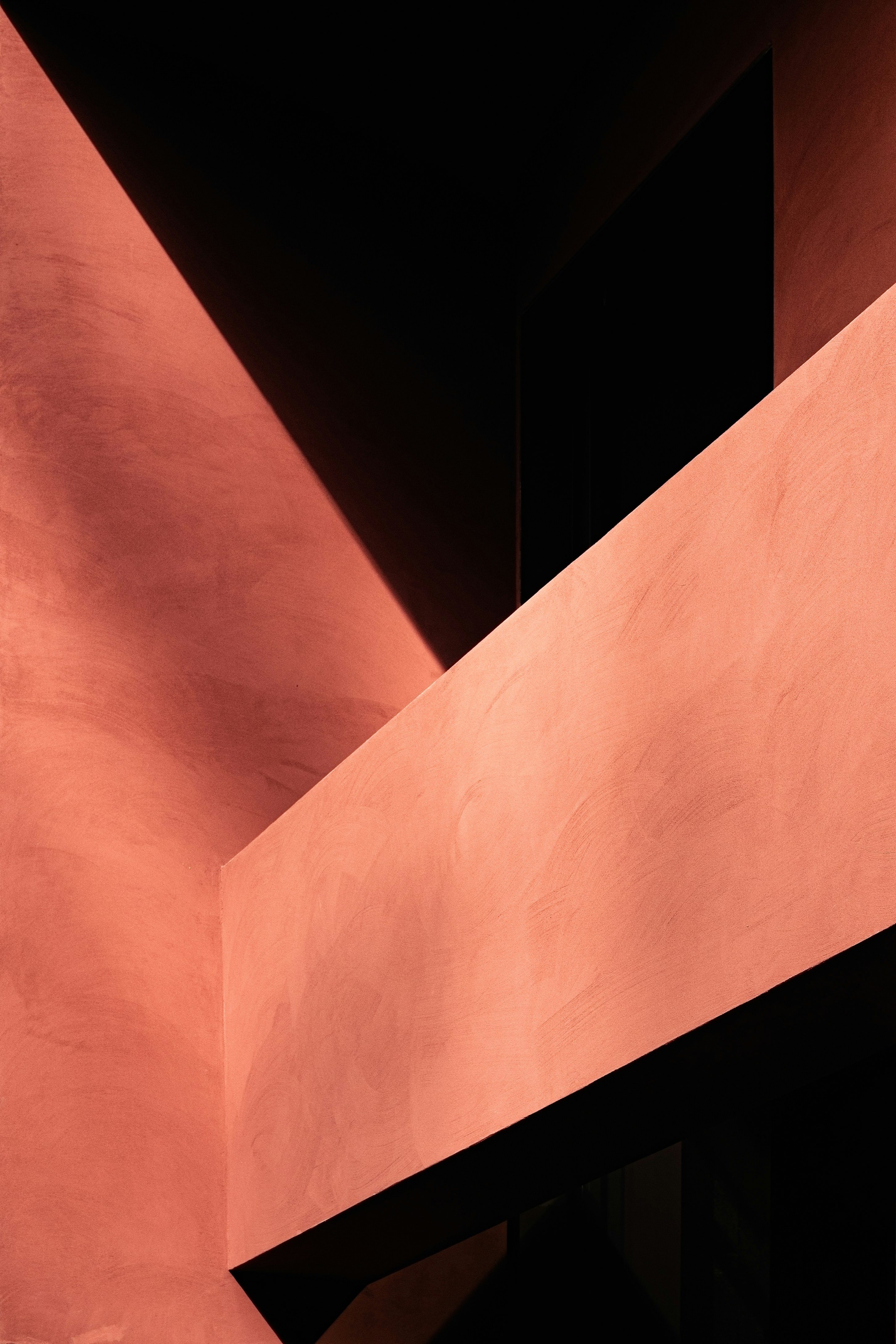 Abstract architectural detail showing intersecting walls and sharp shadows on a terracotta-colored surface.