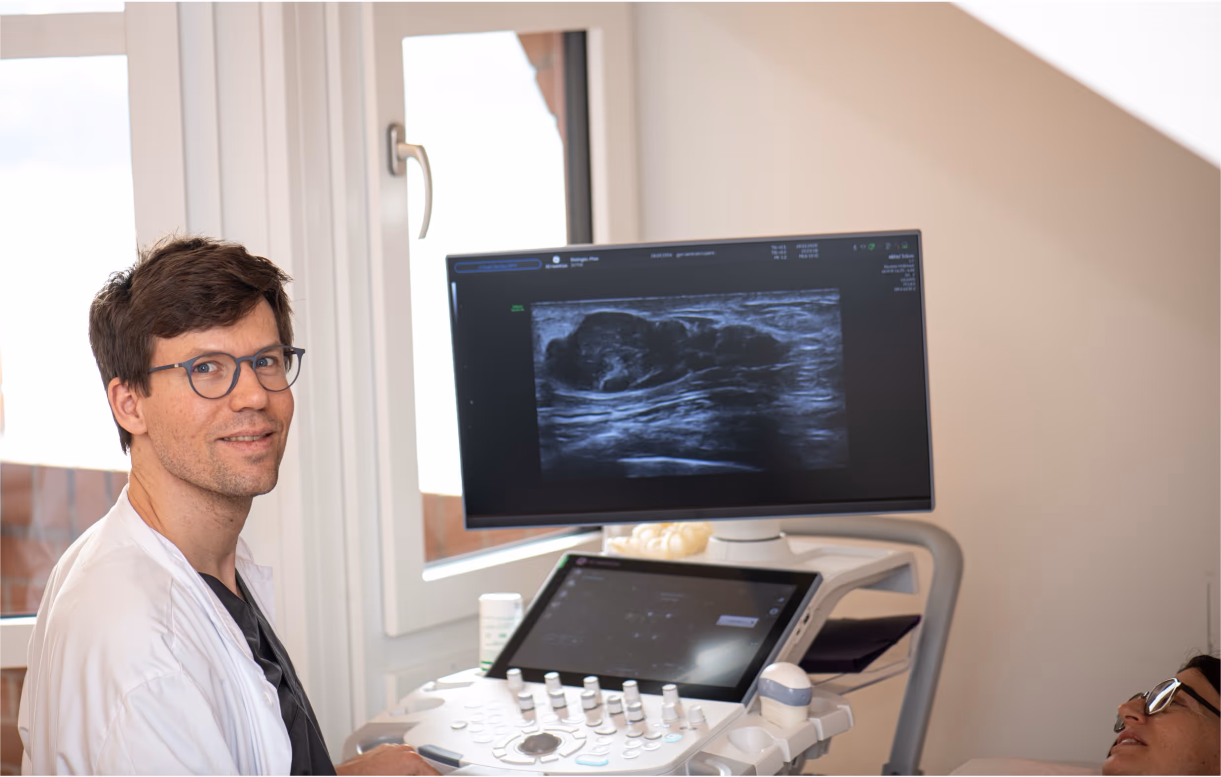 Arzt führt Ultraschalluntersuchung bei einer Patientin durch, Bildschirm zeigt Ultraschallbild.