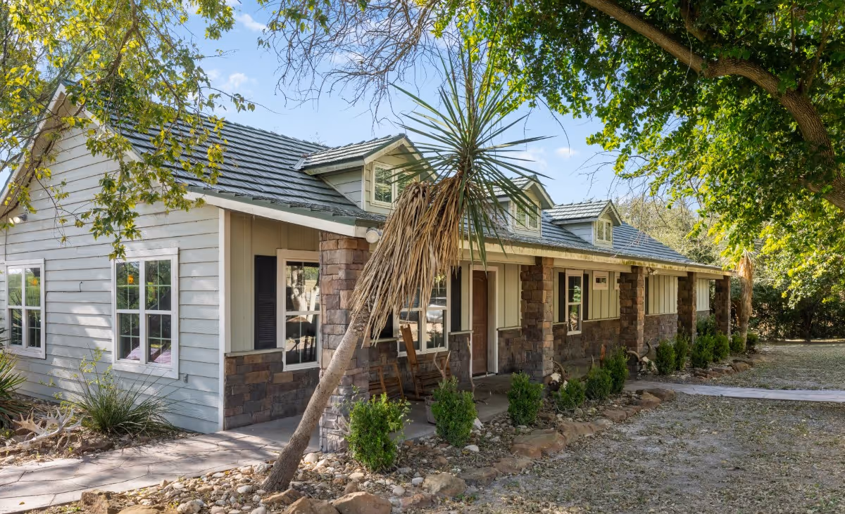 Modern ranch-style house with stone and siding exterior, palm tree, surrounded by green landscaping.