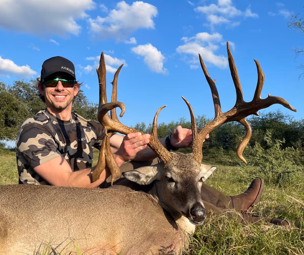 Hunter poses with large buck deer with impressive branching antlers outdoors