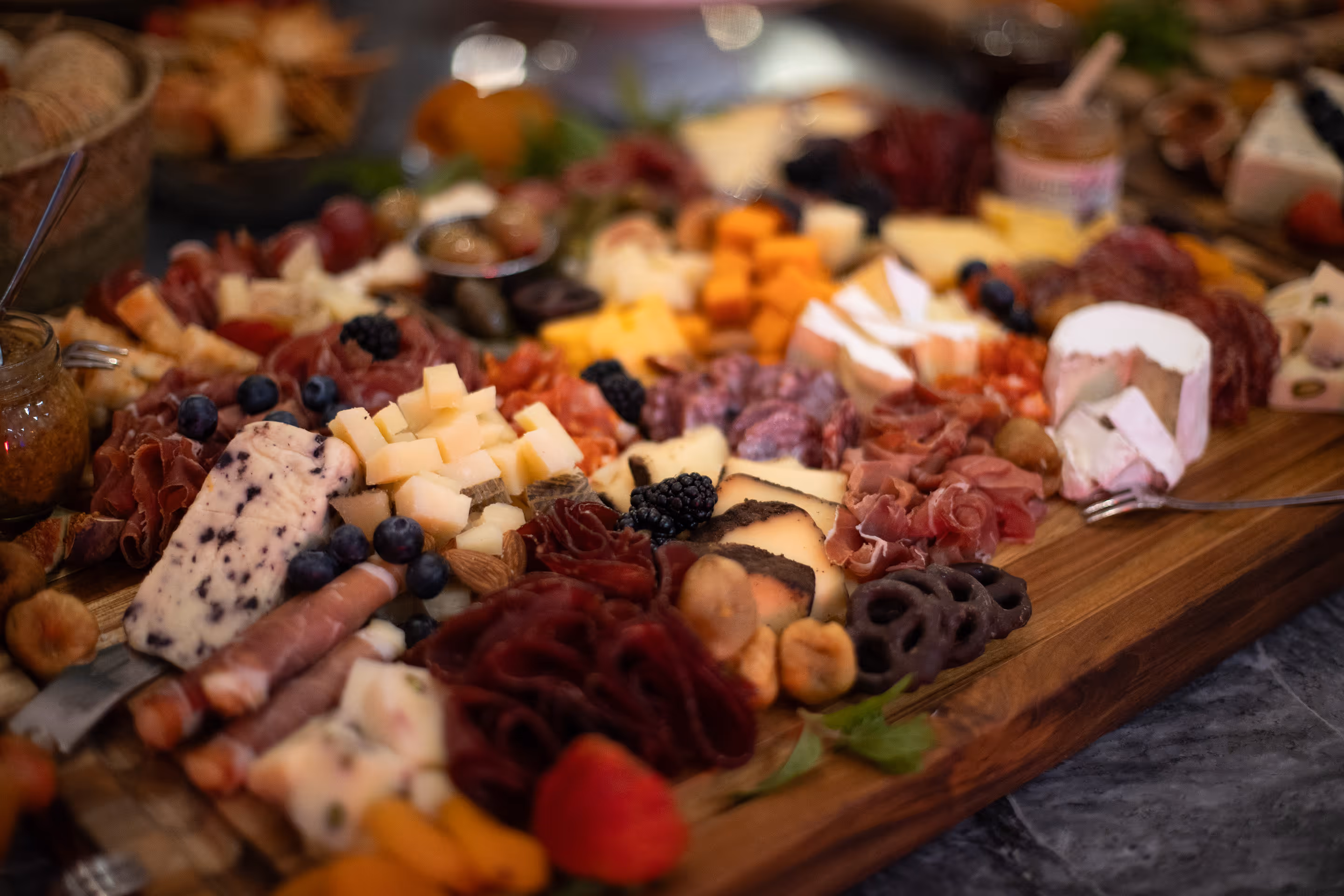 Close-up of an assorted charcuterie board with various cheeses, cured meats, berries, nuts, dried fruits, and chocolate-covered pretzels on a wooden surface.