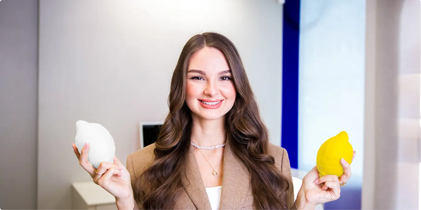 Usměvavá žena s dlouhými vlnitými vlasy drží v jedné ruce bílý citron a v druhé žlutý citron.