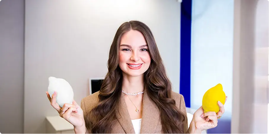 Usměvavá žena s dlouhými vlnitými vlasy drží v jedné ruce bílý a ve druhé žlutý citron.