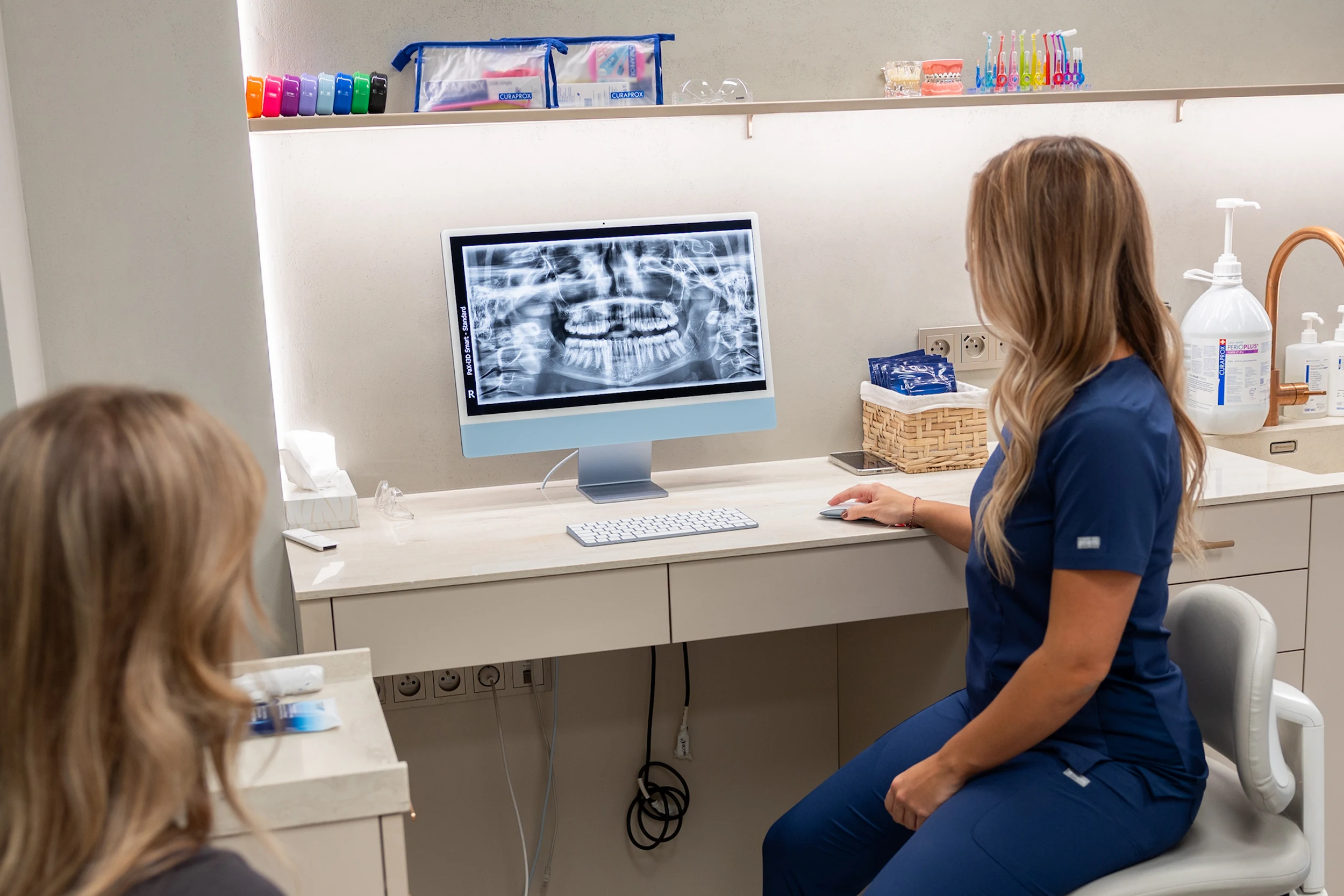 Dentální hygienistka ukazuje pacientce rentgen čelistí na obrazovce počítače v moderní ordinaci.
