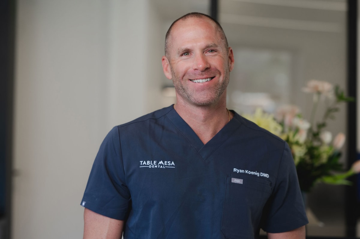 Male dentist in navy scrubs smiling at camera in dental office