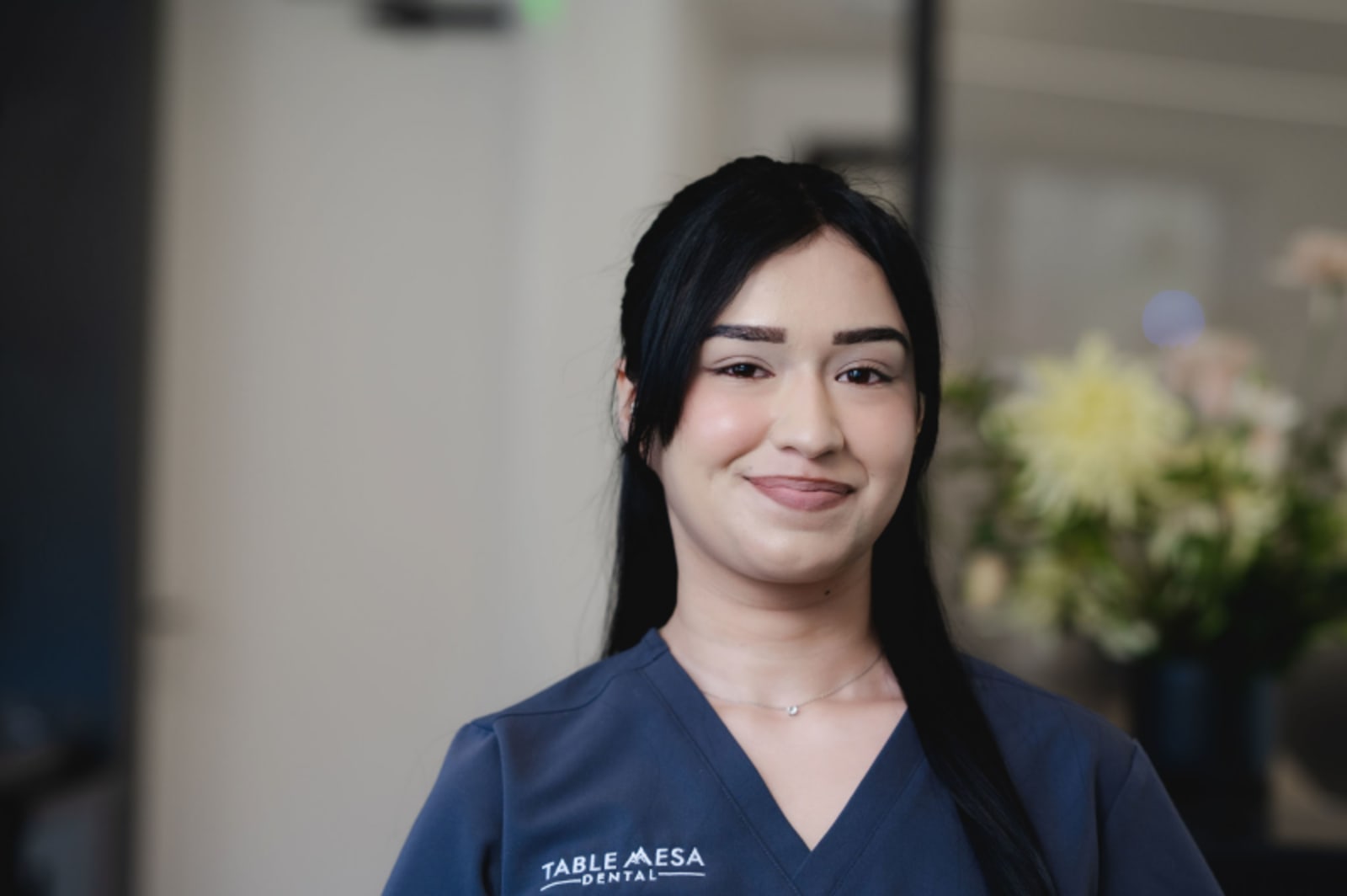 Female dental team member in navy scrubs smiling, representing practice staff