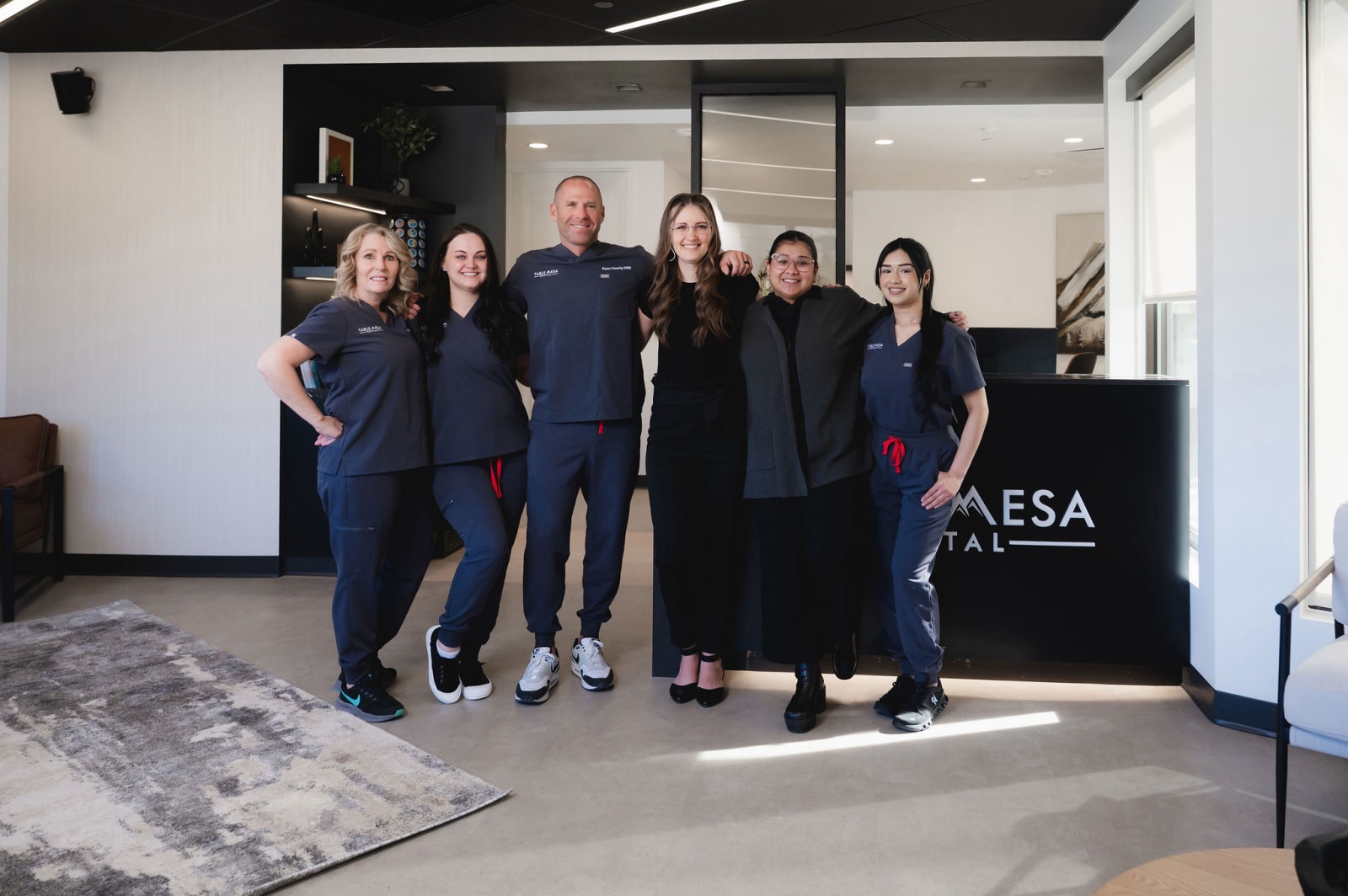 Dental team of five professionals standing together in modern operatory with Table Mesa signage