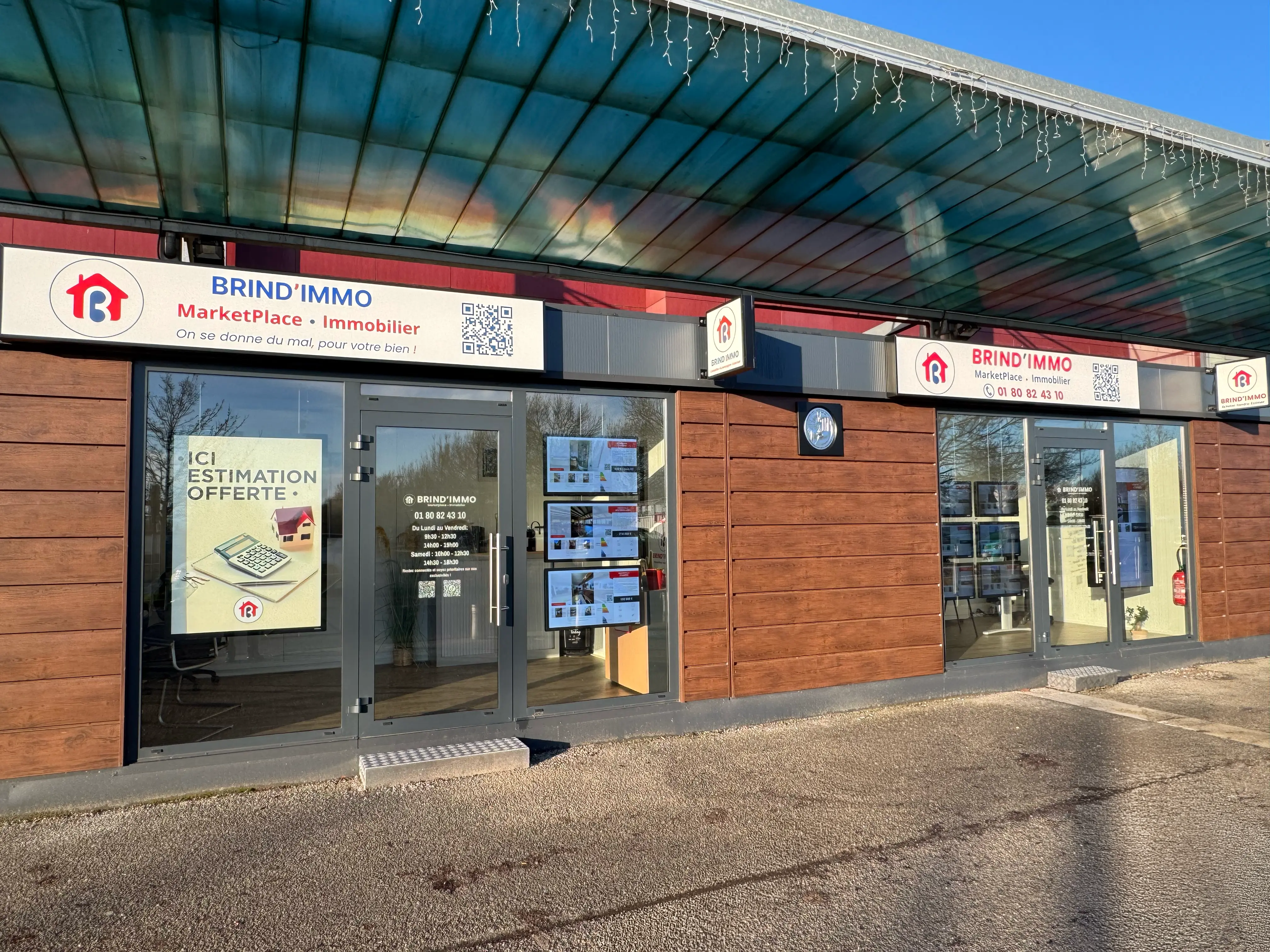 Façade d'une agence immobilière Brind'Immo avec panneaux en bois, vitrines affichant des offres immobilières et enseignes visibles sous un auvent.
