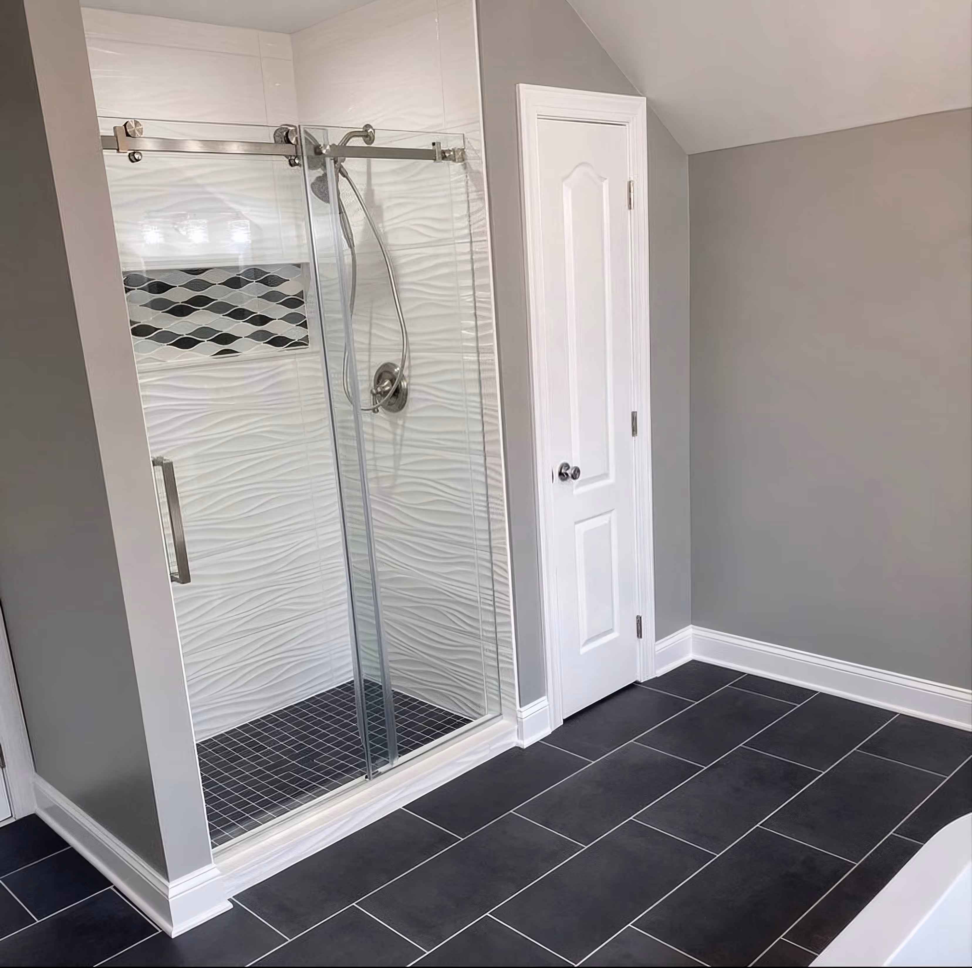 Modern bathroom with glass shower, wavy white tile walls, black tile floor, and closed white door.