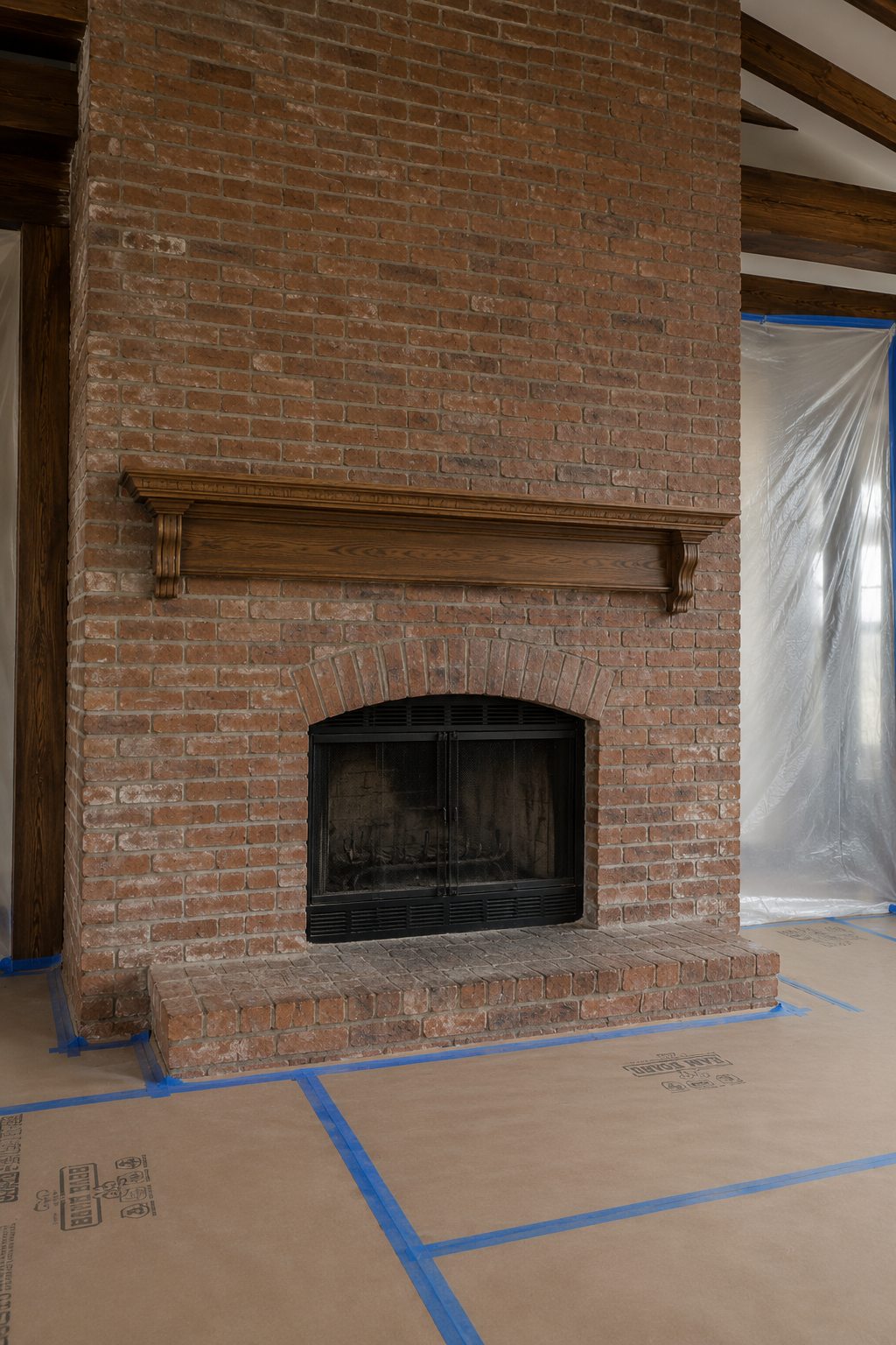 Full-height dated brick fireplace with an older wood mantel and protective floor covering before renovation.