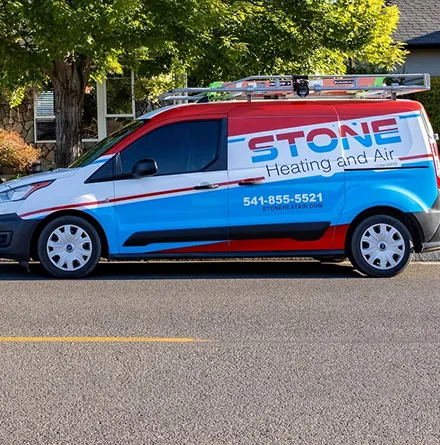 Red, white, and blue service van with ladder on roof, labeled 'Stone Heating and Air' with phone number 541-855-5521 parked on a street.
