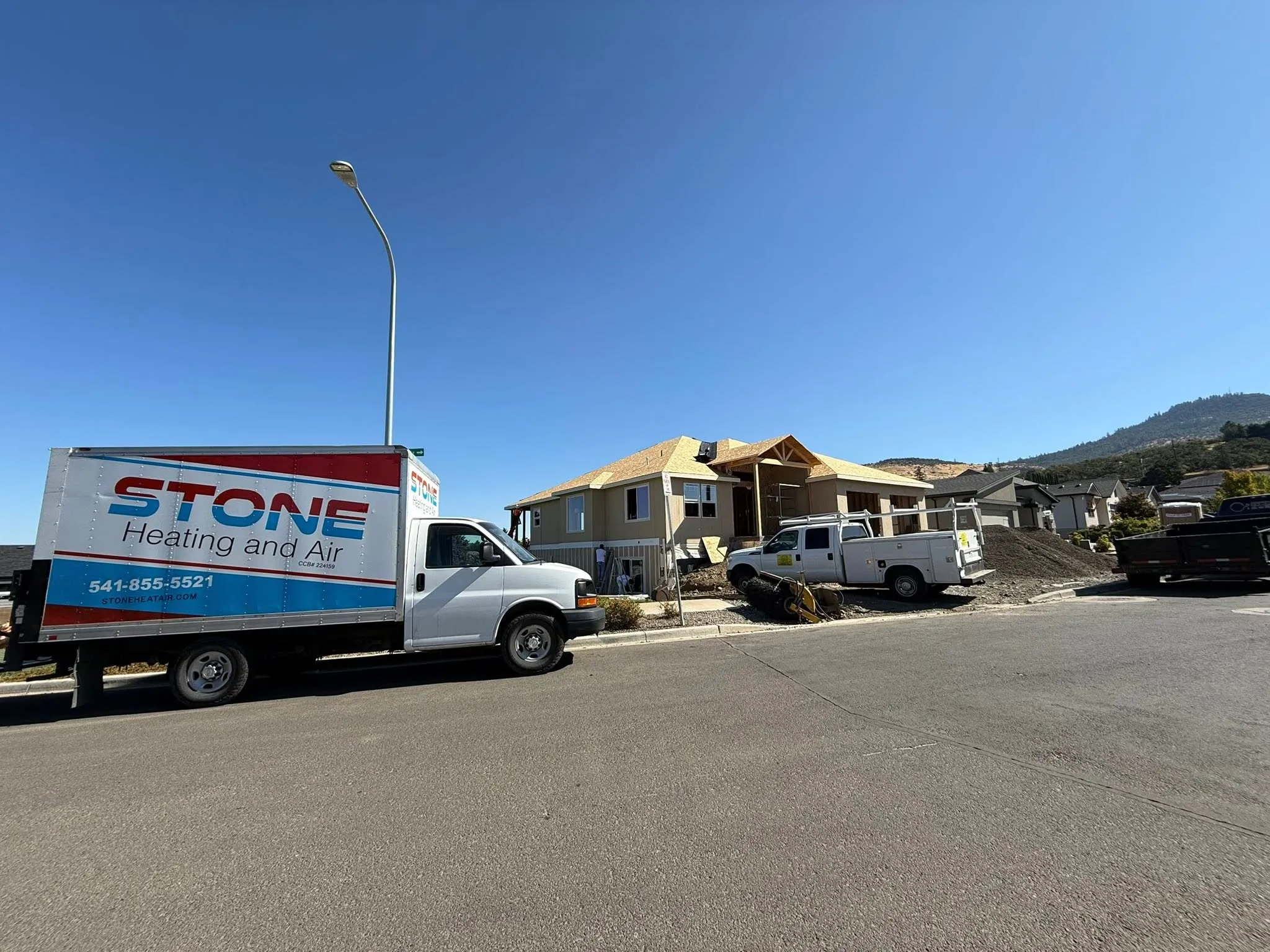 Stone Heating and Air service truck parked on street near a house under construction with construction vehicles and materials outside.