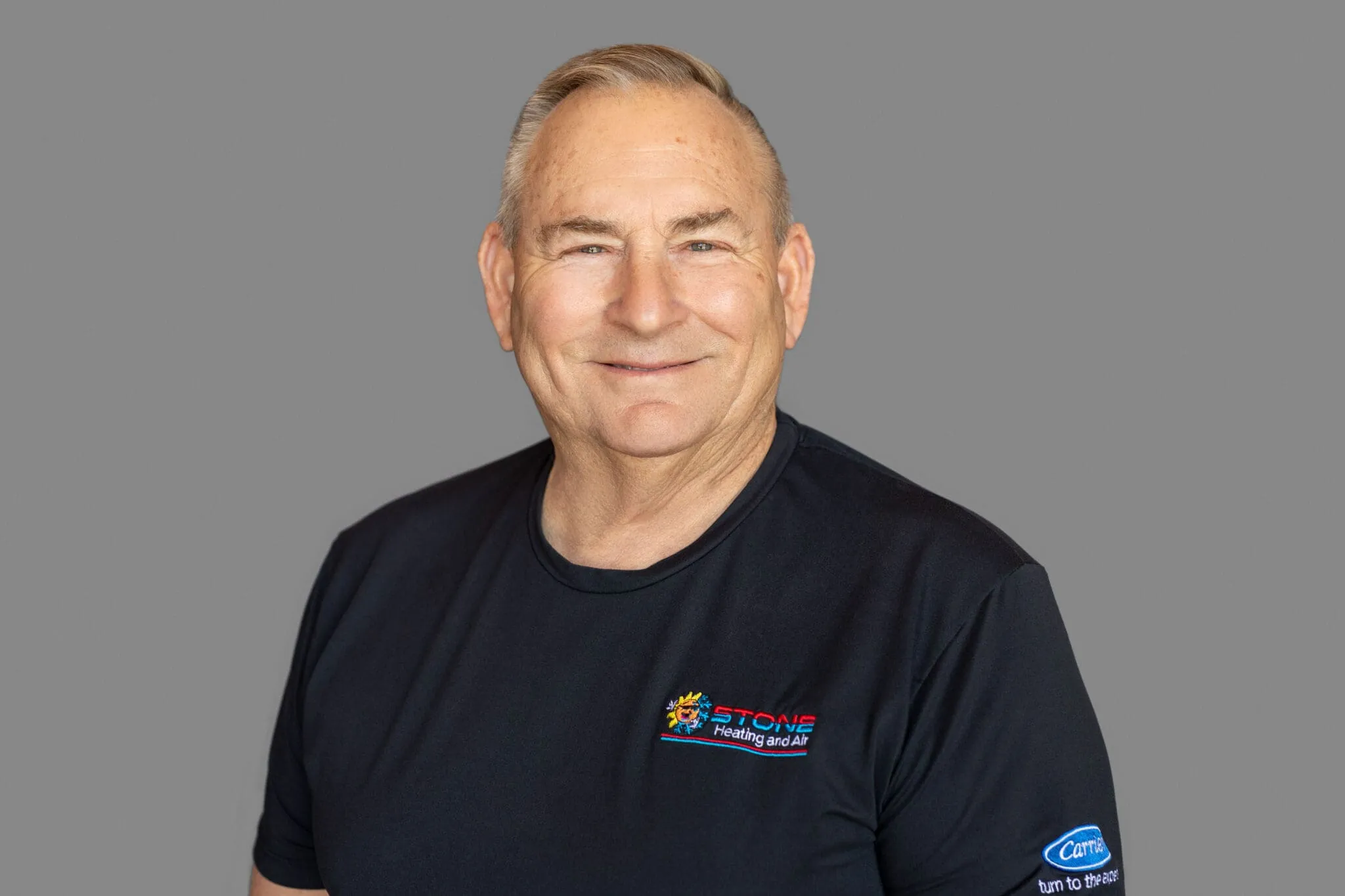 Smiling older man wearing a black Stone Heating and Air t-shirt with a gray background.