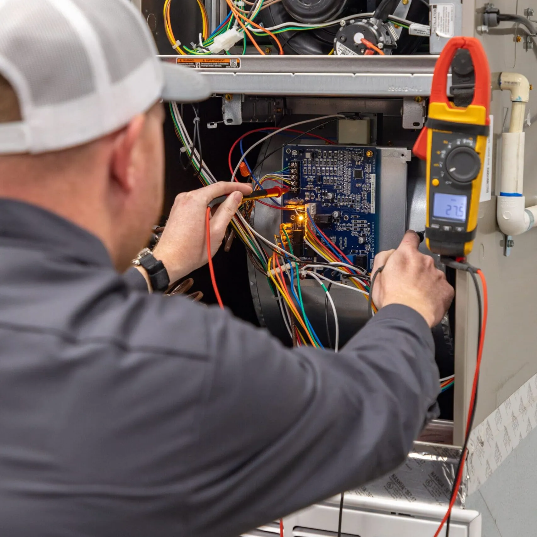Technician using a multimeter to test wiring on an open electrical control panel with colorful wires.
