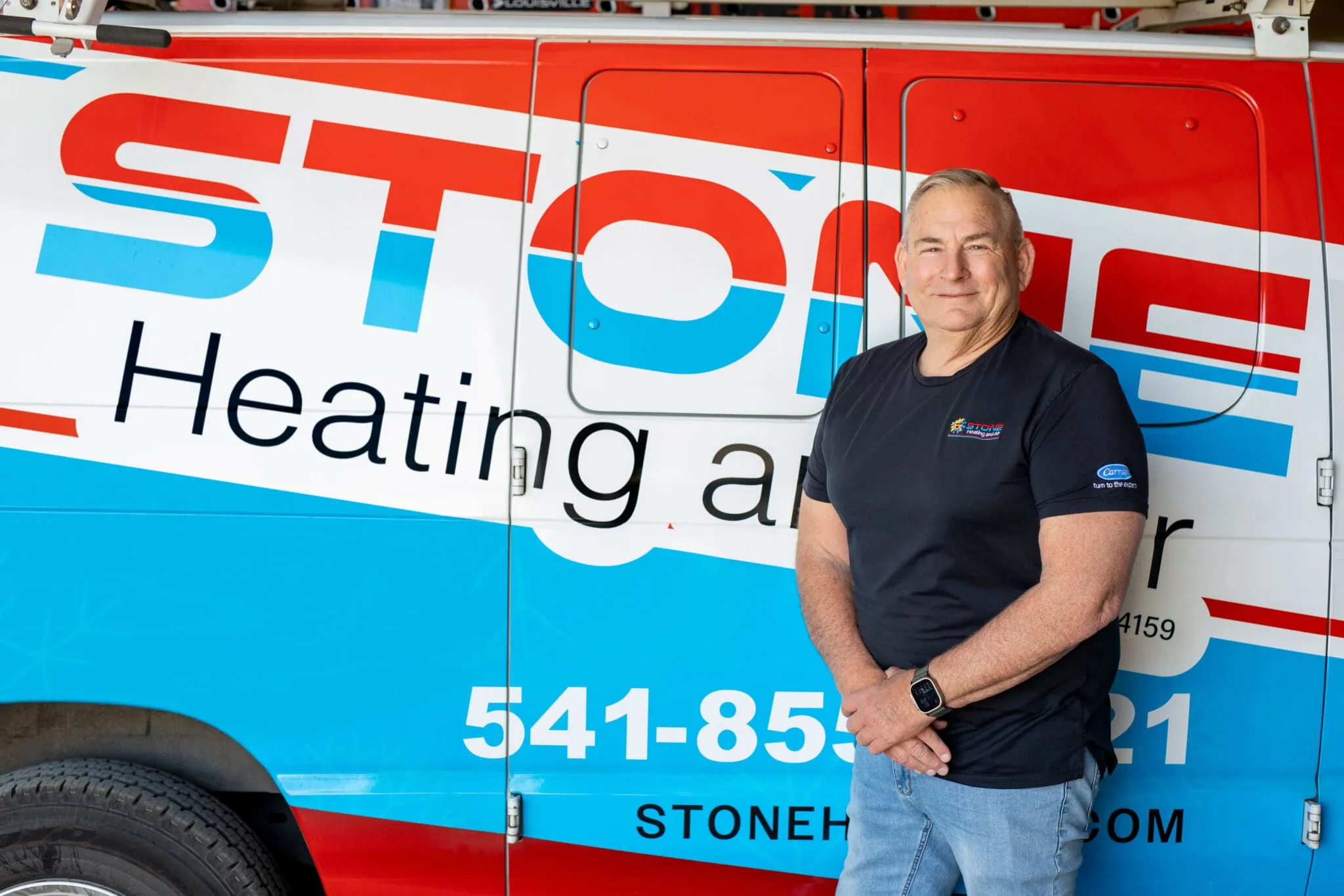 Man in black shirt standing and smiling in front of a Stone Heating and Air van.