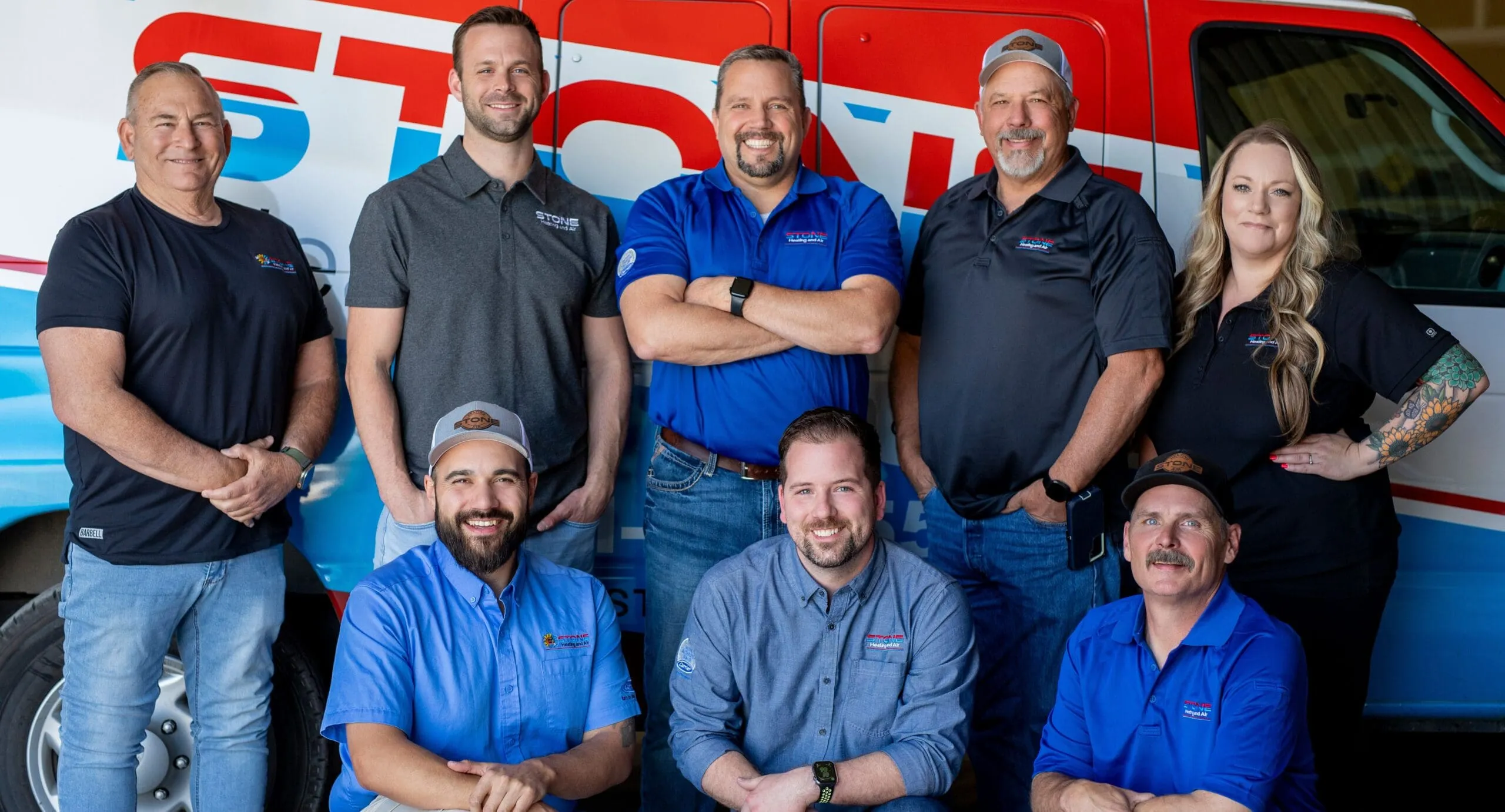 Group photo of eight smiling employees in company uniforms posing in front of a red and white branded service van.