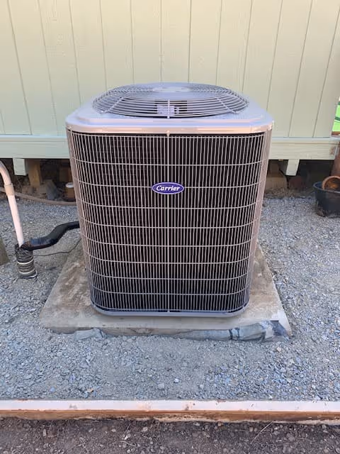 Carrier brand outdoor air conditioning unit installed on a concrete pad surrounded by gravel.