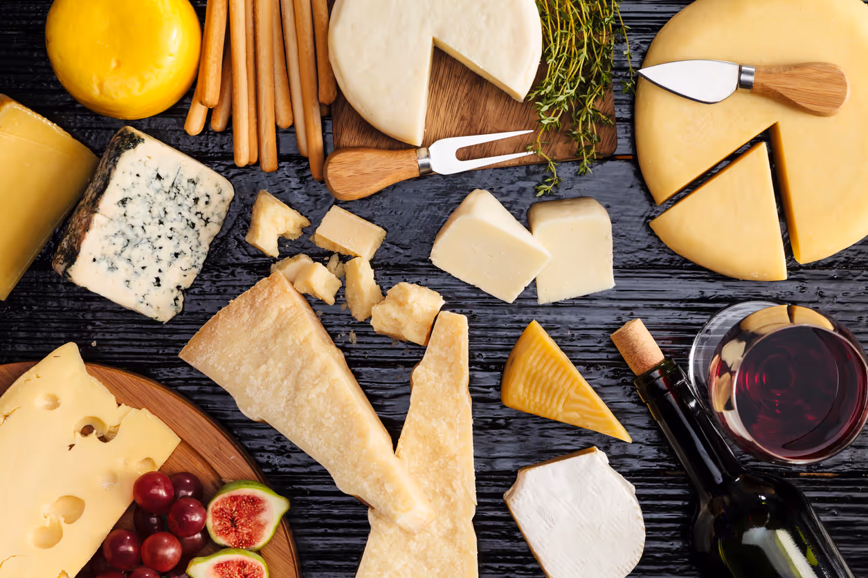 Assorted cheese varieties including wedges, blocks, and wheels with wine and herbs