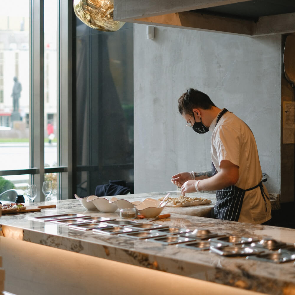 Chef wearing a mask and gloves preparing dough on a marble countertop in a modern kitchen.