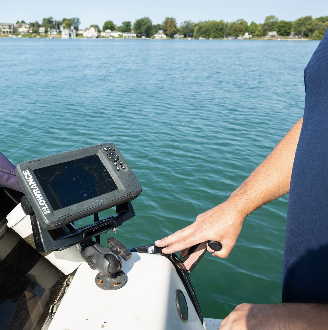 Person operating boat throttle next to a mounted Lowrance fish finder screen on a lake.