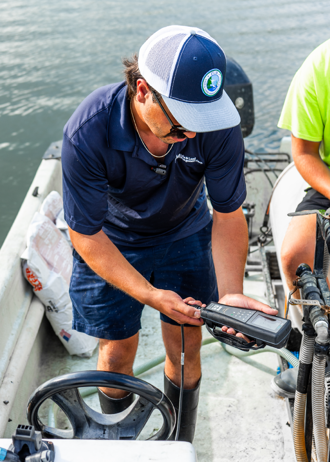 Man in navy blue shirt and cap using a handheld water quality testing device on a boat.