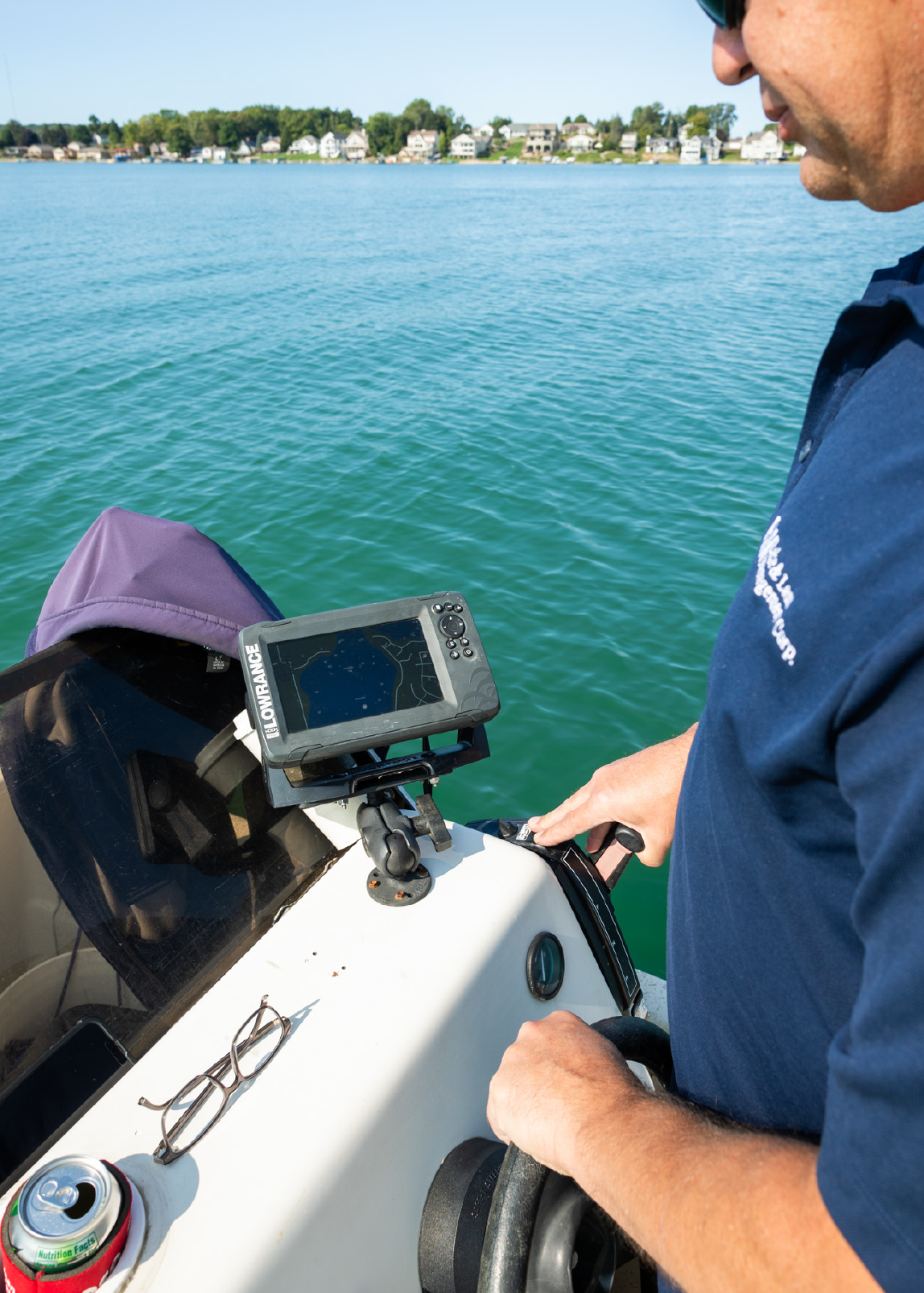 Person steering a boat on calm water with a Lowrance fish finder and glasses on the console.