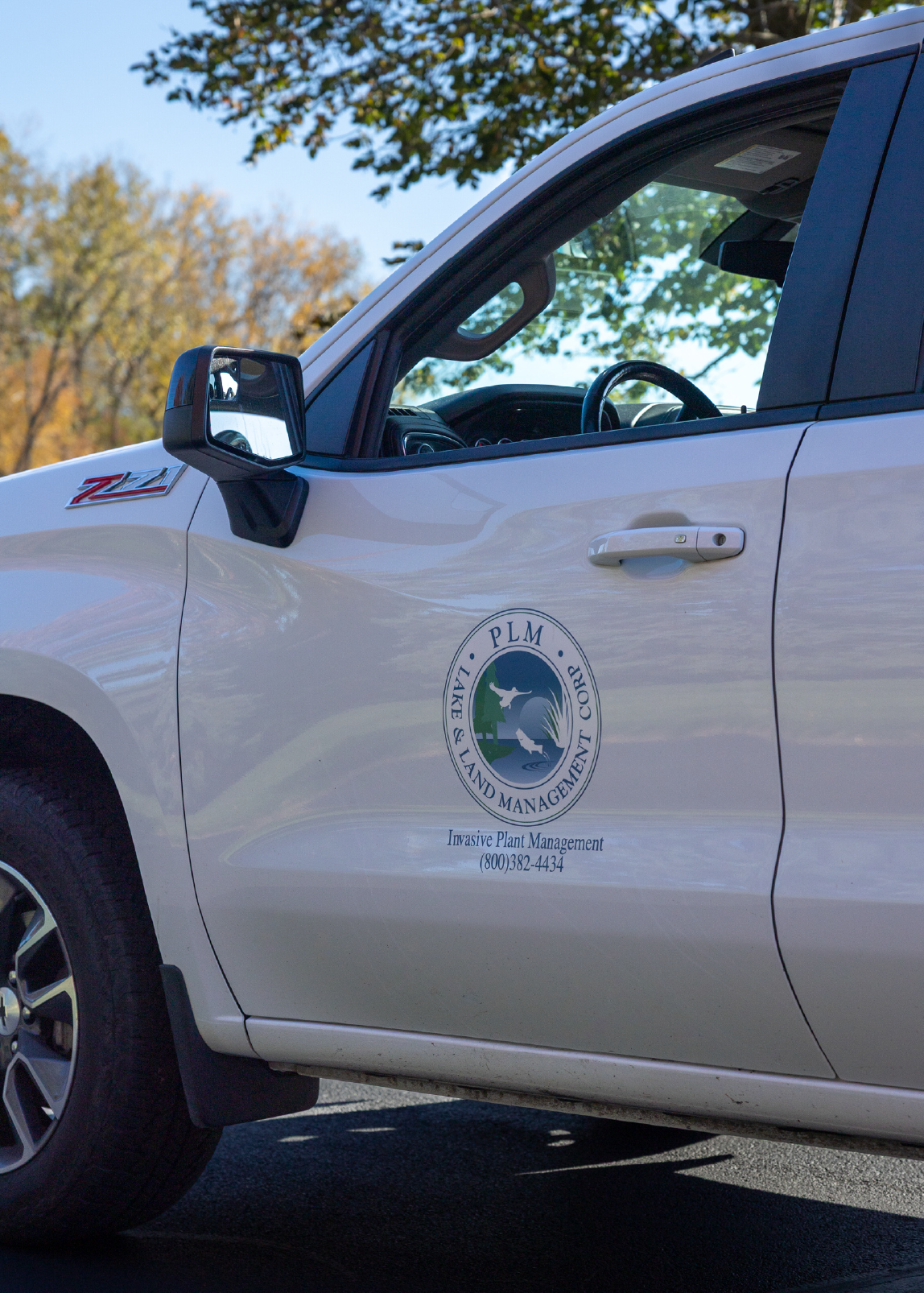 White pickup truck with PLM Lake & Land Management Corp logo and contact info on the door.