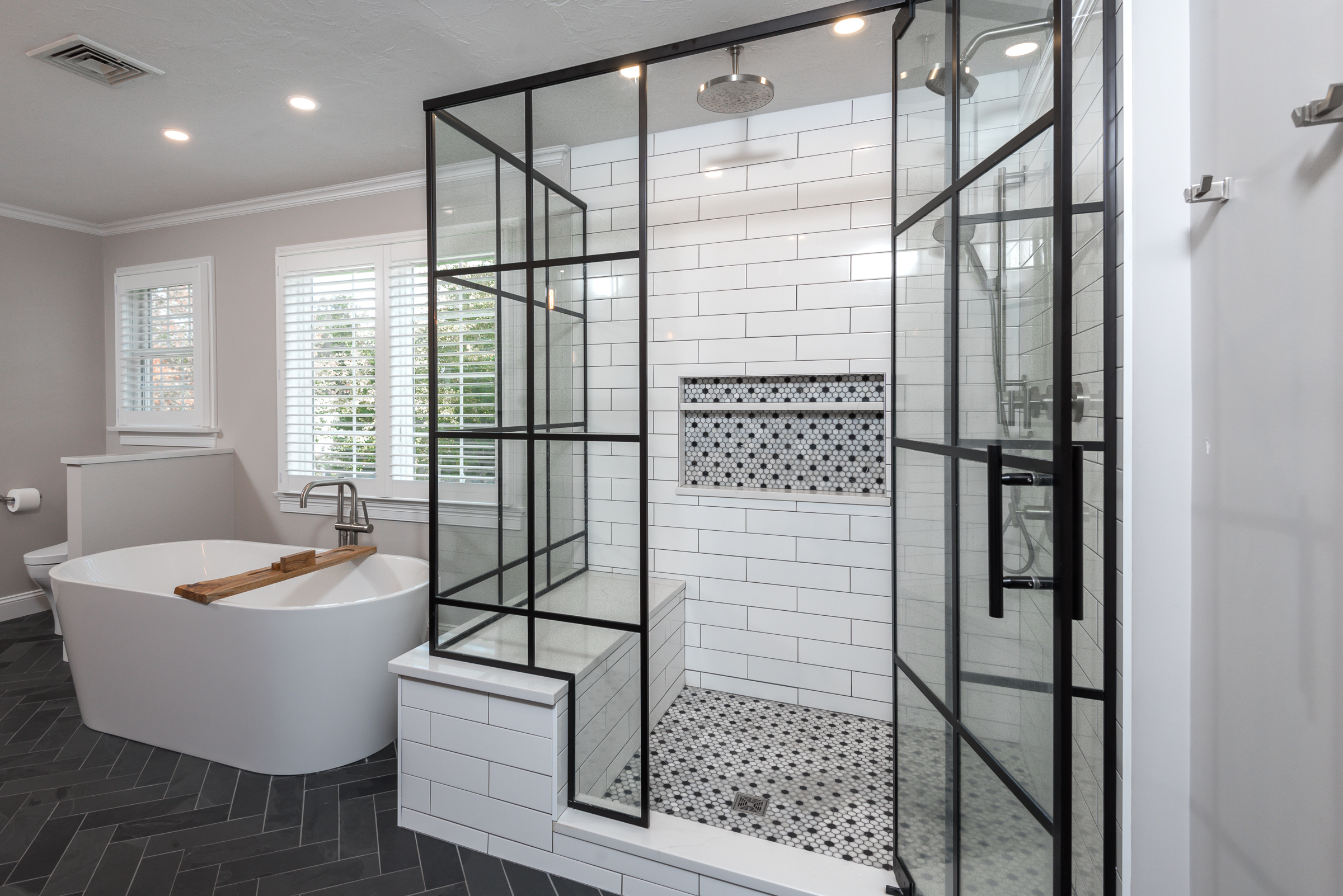 Modern bathroom with a freestanding bathtub, large walk-in shower with black-framed glass enclosure and white subway tile walls.