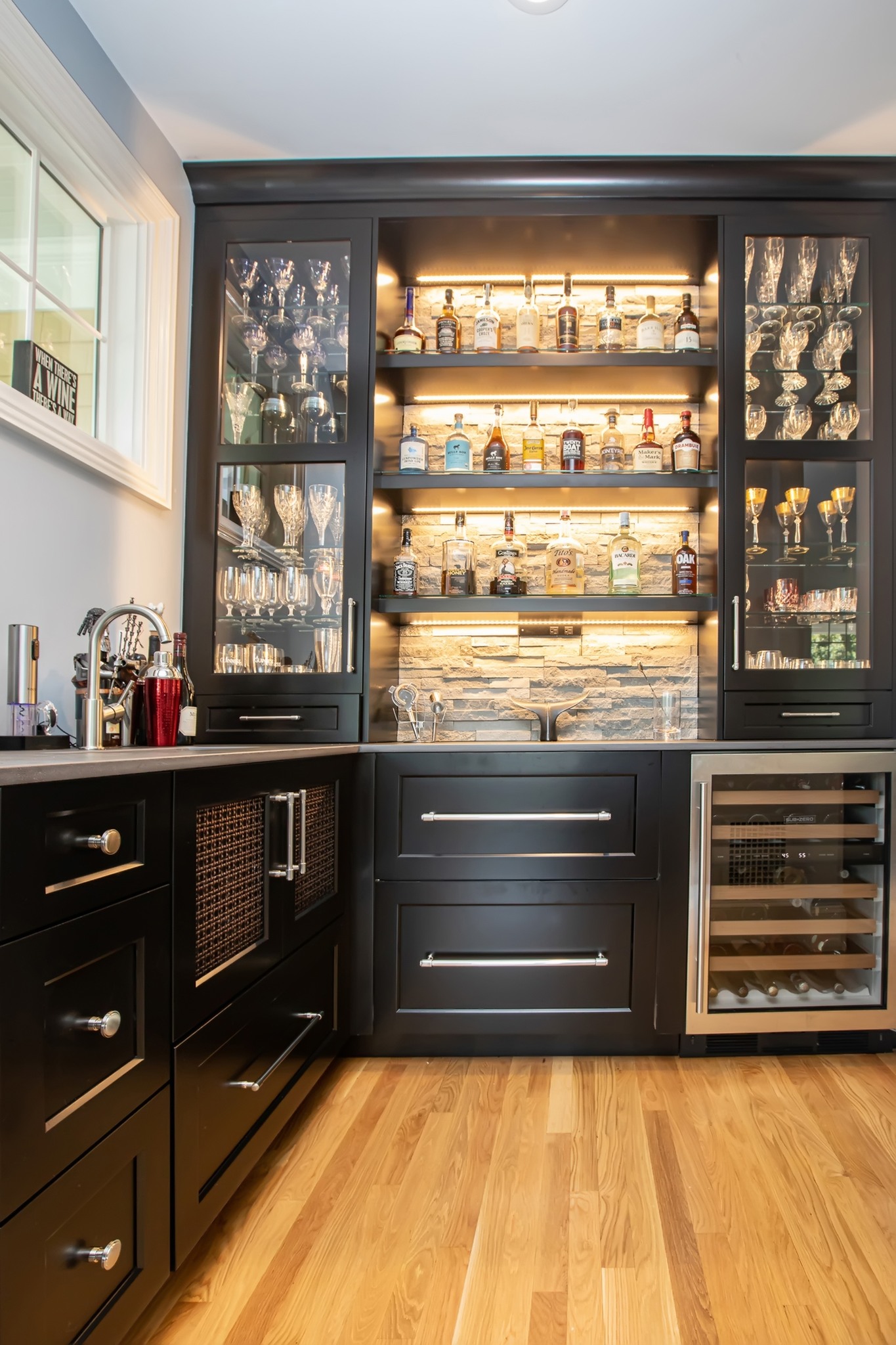 Home bar with glass-front upper cabinets, illuminated shelving, and dark lower cabinetry.