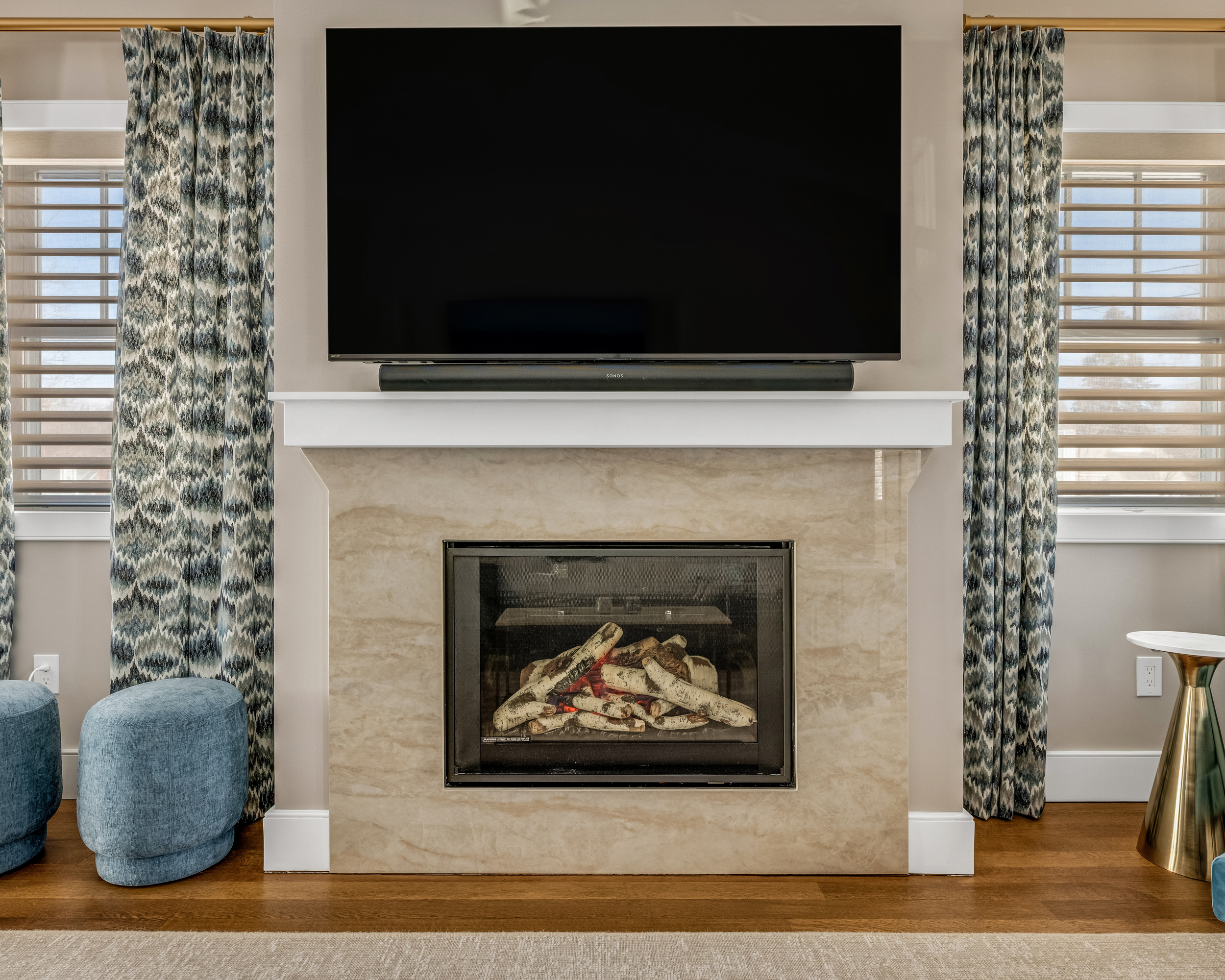 Stone fireplace surround with white mantel and patterned drapery in a living room.
