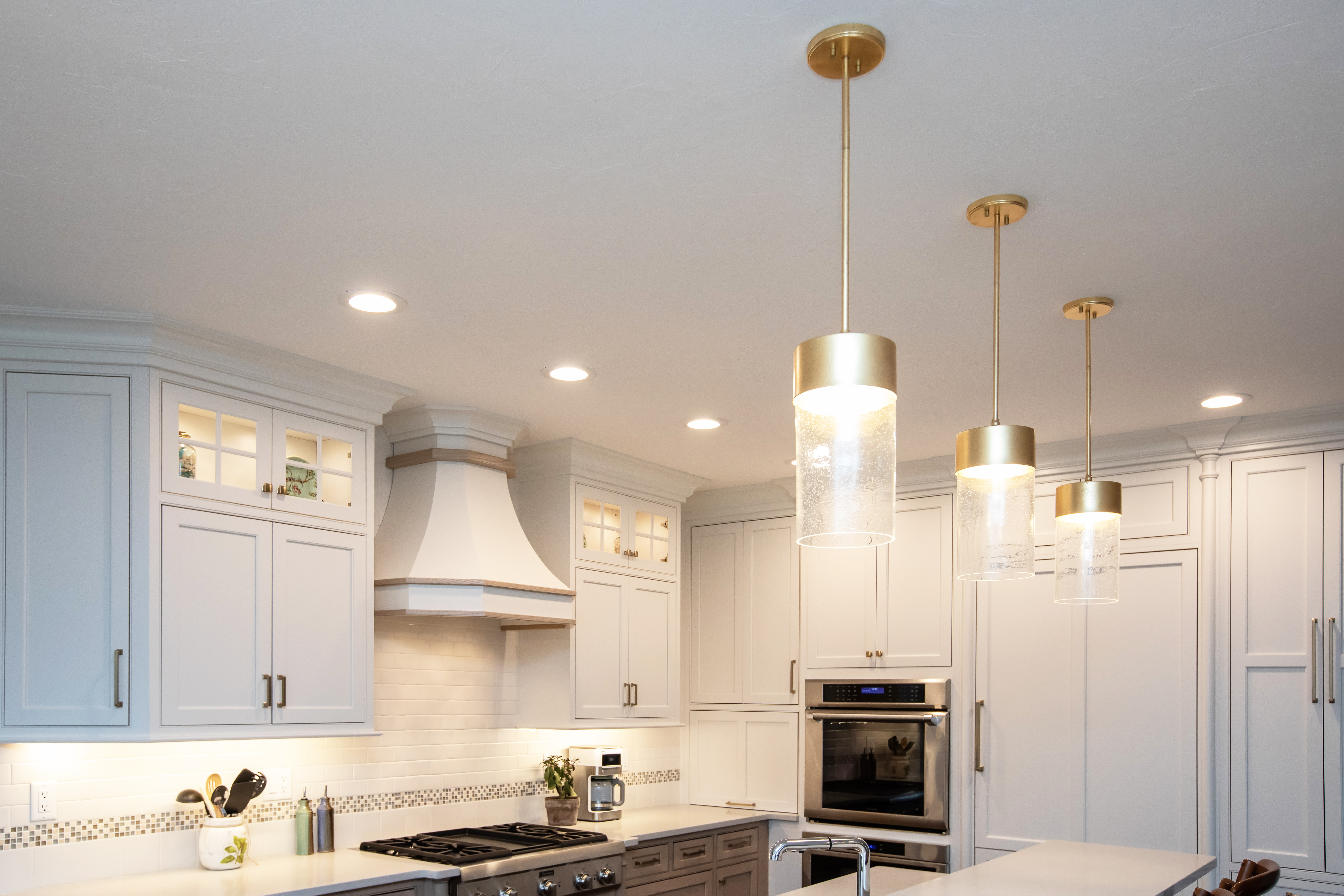 Modern kitchen with white cabinetry, stainless steel oven, a gas stove, and three hanging pendant lights with gold accents.