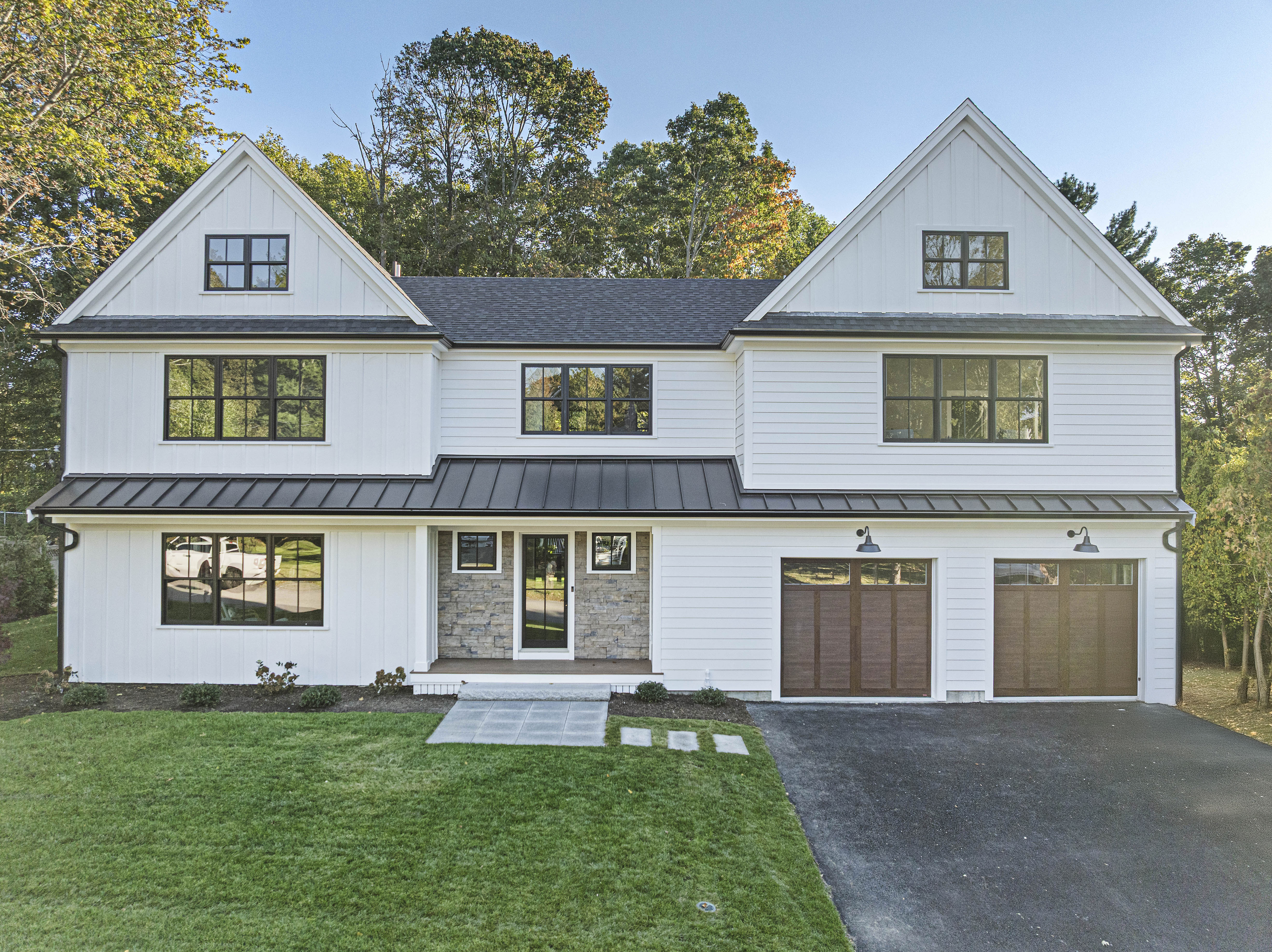 White two-story house with black-framed windows, stone accent around the front door, two wooden garage doors, and a green lawn.