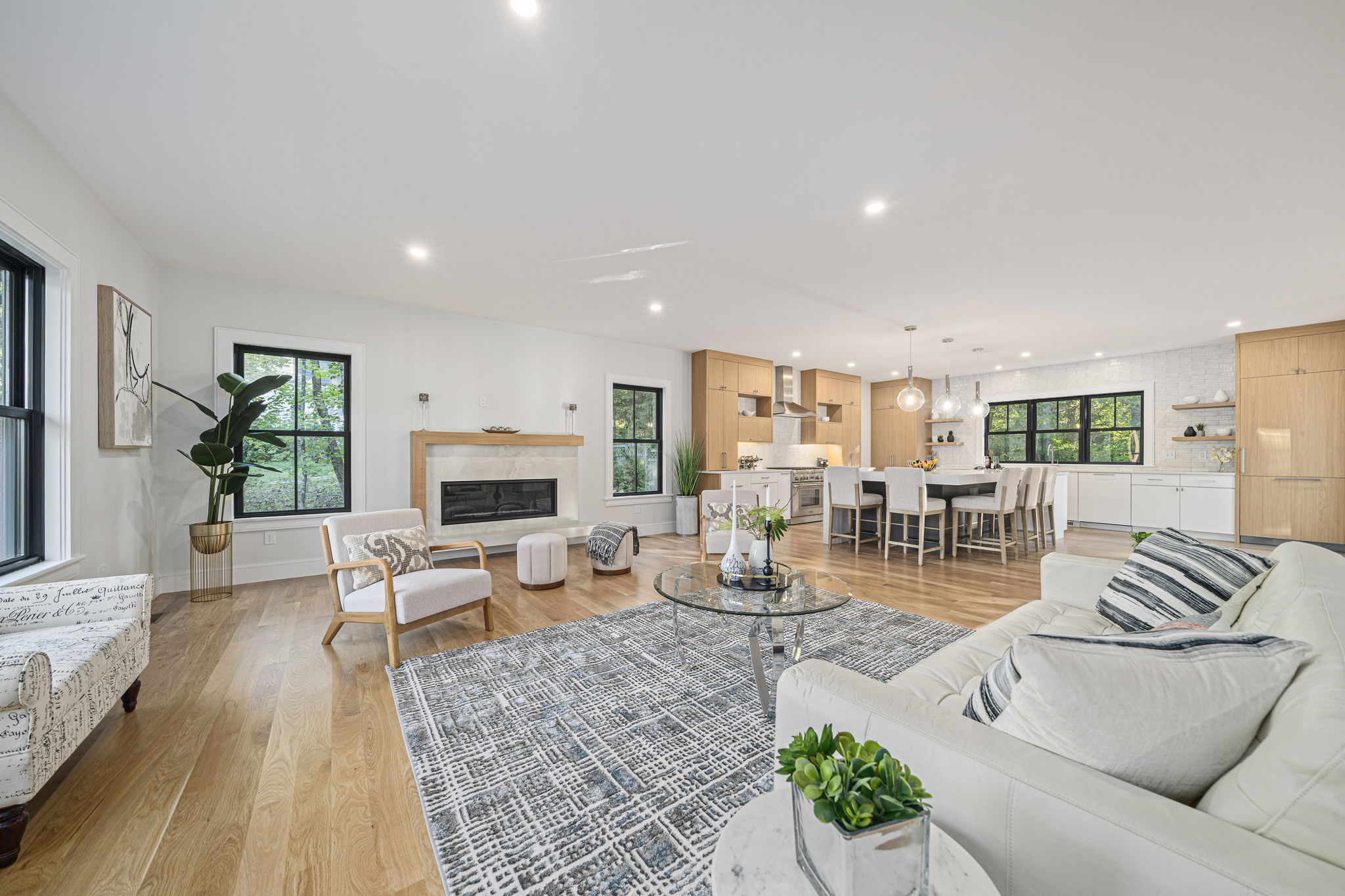 Spacious open living room and kitchen with light wood floors, white walls, modern fireplace, and large windows.