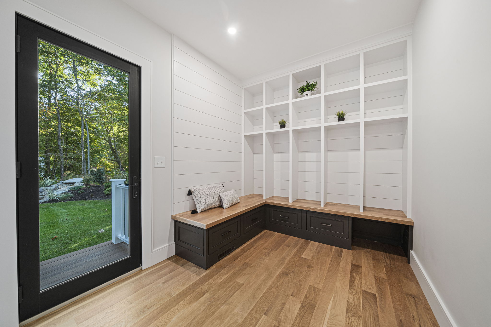 Modern mudroom with built-in black storage bench, white open shelves, wooden countertop, and glass door showing green backyard.