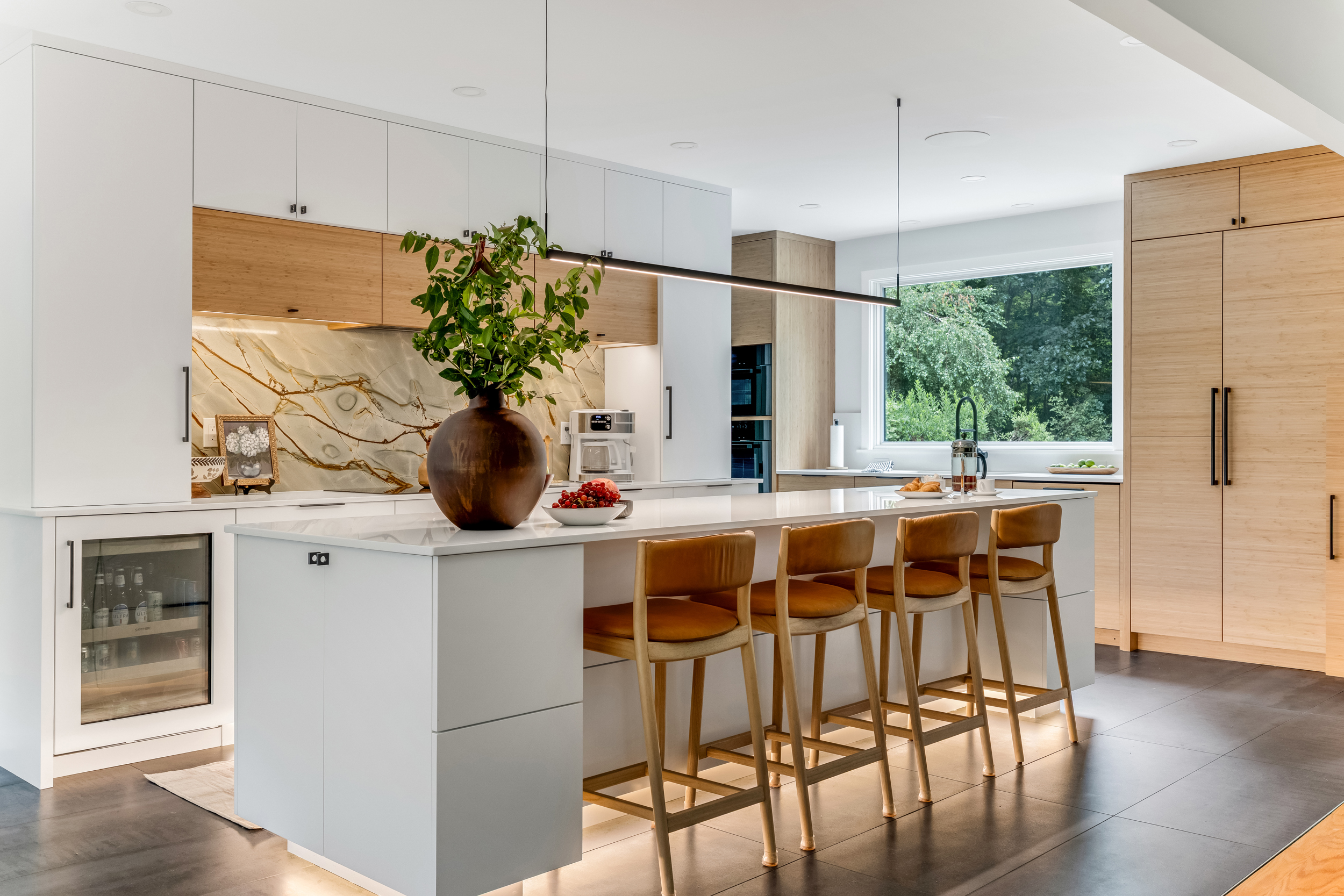 Modern kitchen island in white quartz with leather counter stools, beverage fridge, white oak pantry cabinets, and a linear pendant light