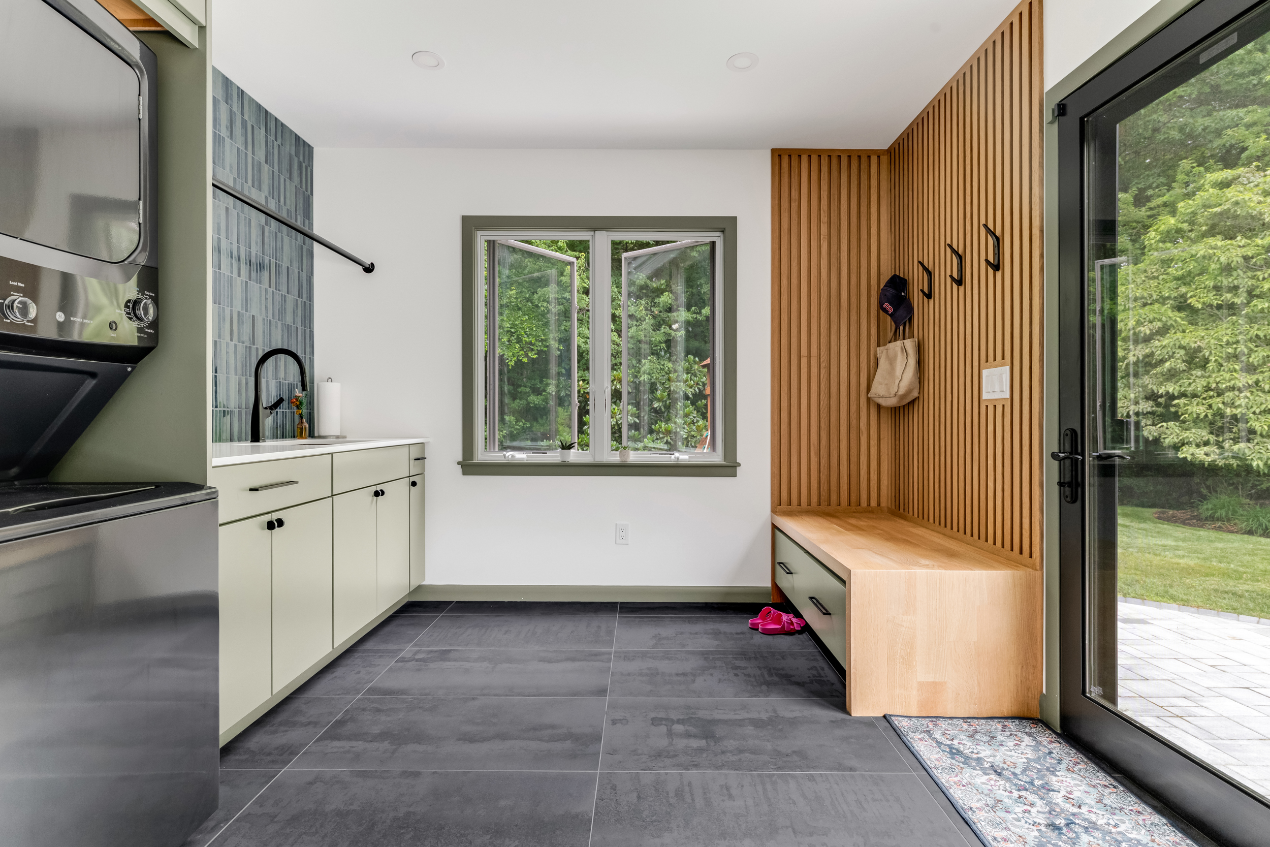 Marshfield mudroom and laundry addition with a rift-sawn white oak slat wall and bench, green Diamond cabinetry, blue-green tile backsplash, laundry sink, and stacked washer and dryer
