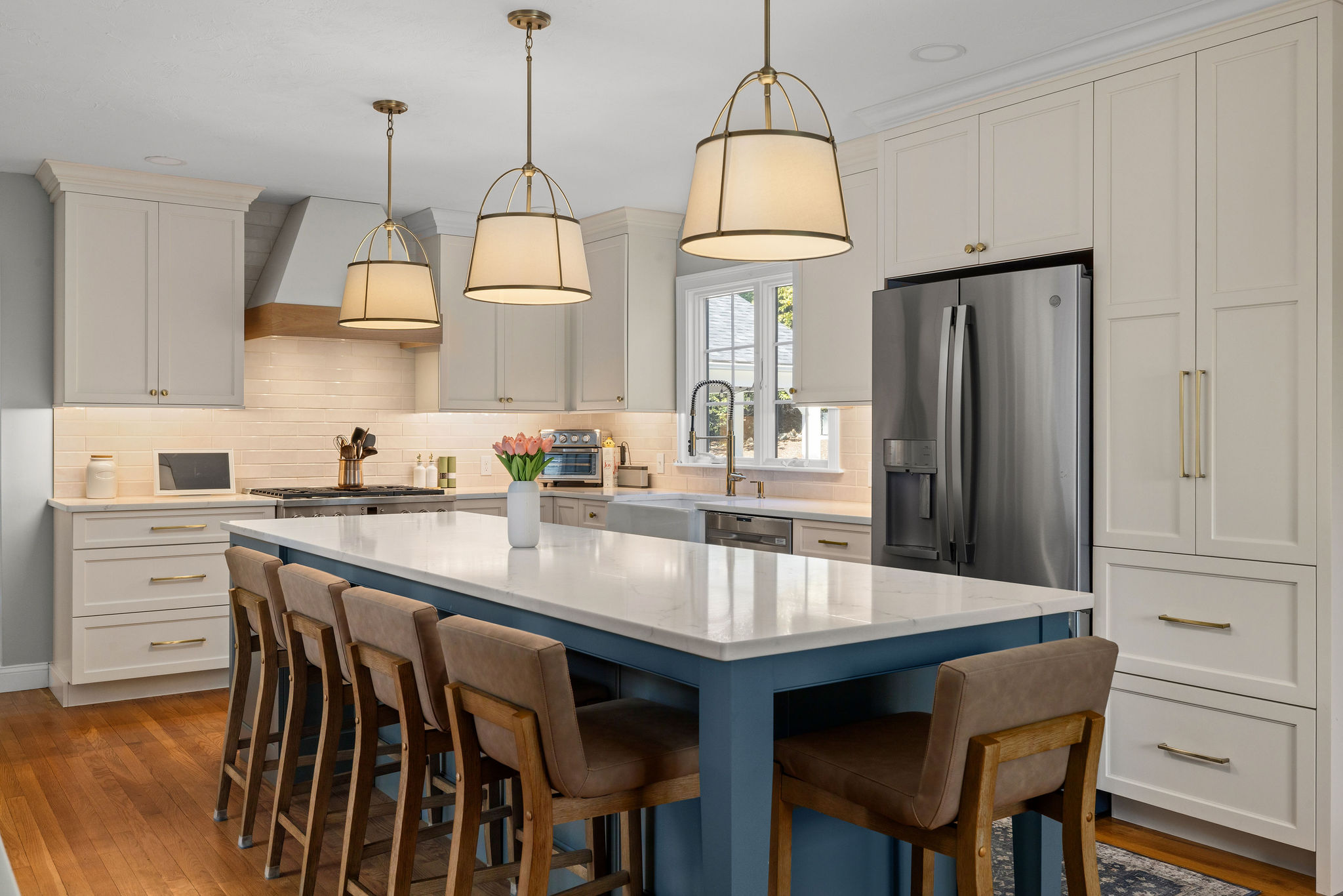 Modern kitchen with cream and teal cabinets, a marble island with a flower vase, stainless steel oven, and brass hardware.