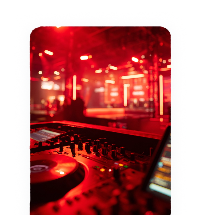 Close-up of a DJ mixing console with red stage lighting and blurred background of a concert venue.