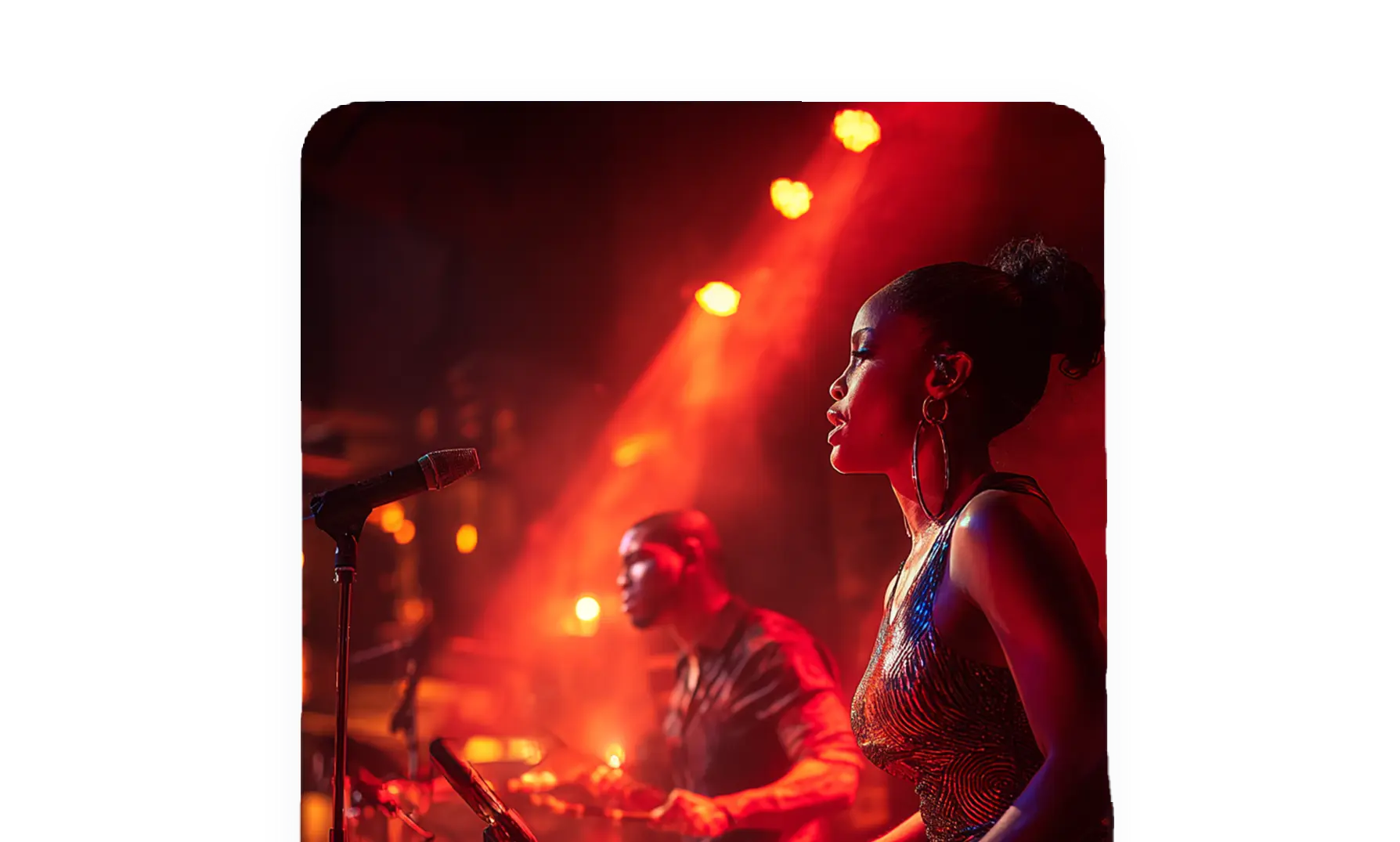 Female singer and male drummer performing on stage with warm red and orange stage lighting.