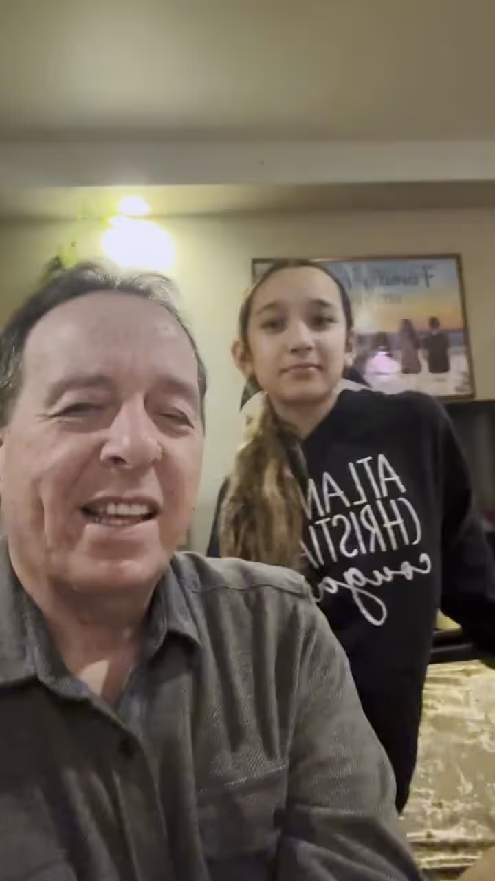 Man and young girl smiling at church or hospital event with framed picture in background.