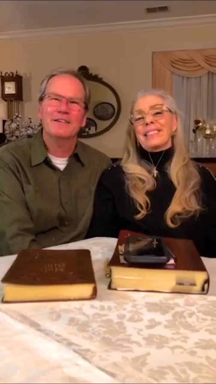 Couple sitting at table with Bibles, smiling and looking forward in a church setting.