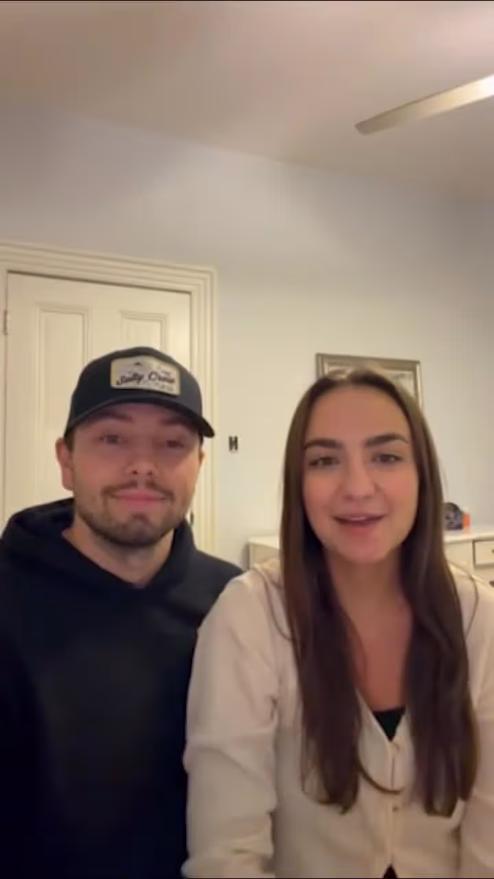 Man and woman smiling at camera in a room with white walls and door.