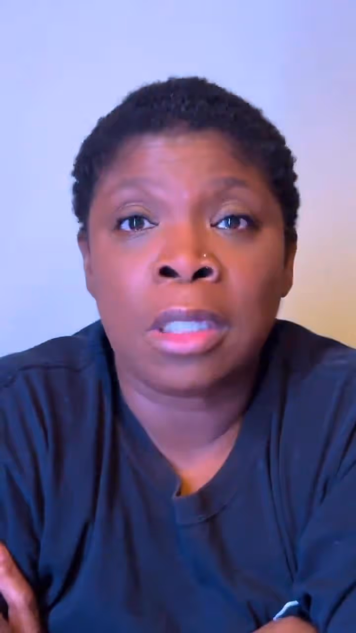 Woman in dark blue hospital scrubs with short hair looking directly ahead with a serious expression.