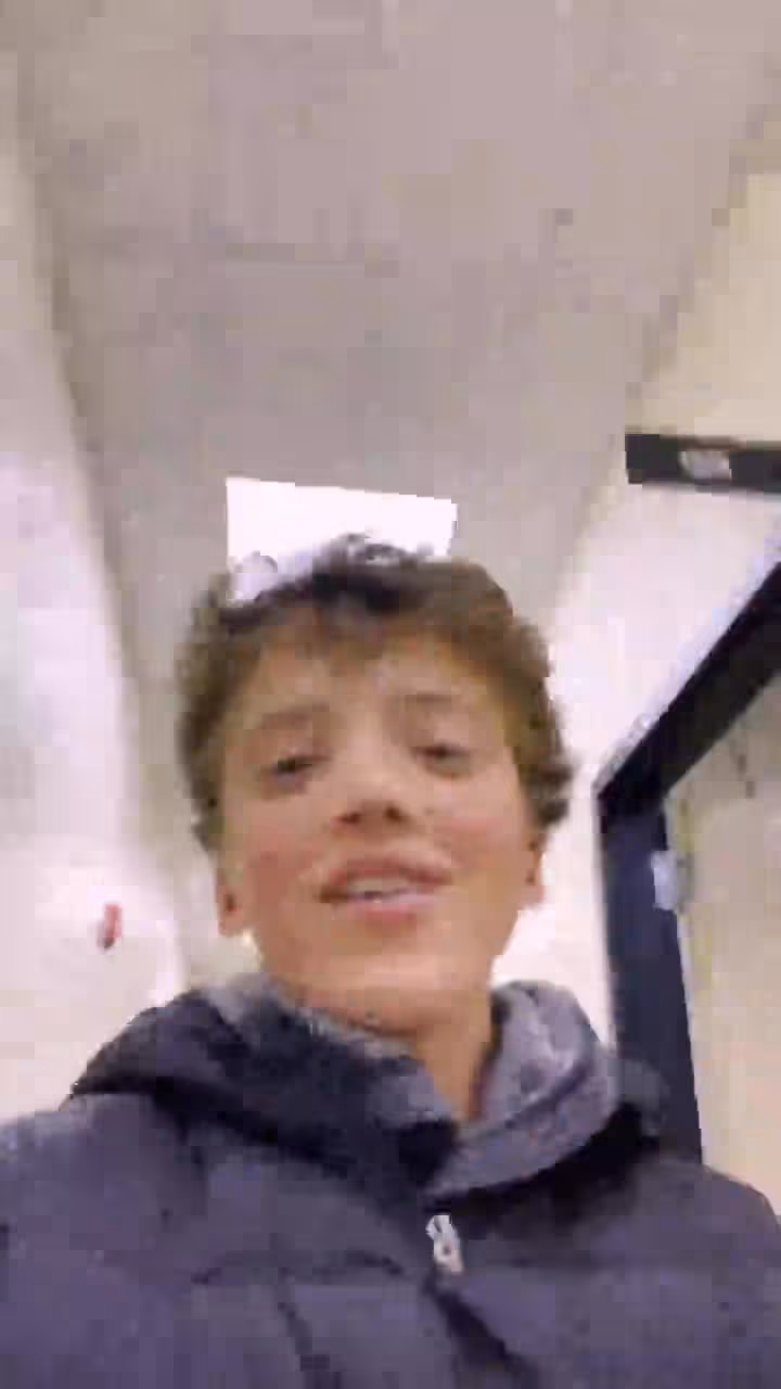 Young boy smiling in hospital or church hallway wearing dark blue jacket.