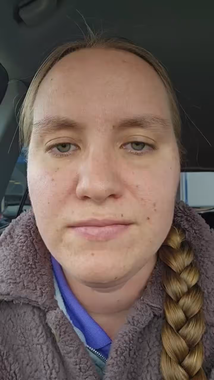 Woman with green eyes and braided hair sitting in a vehicle, wearing a fleece jacket.