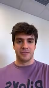 Young man with short brown hair wearing purple shirt with black text in hospital or church setting.