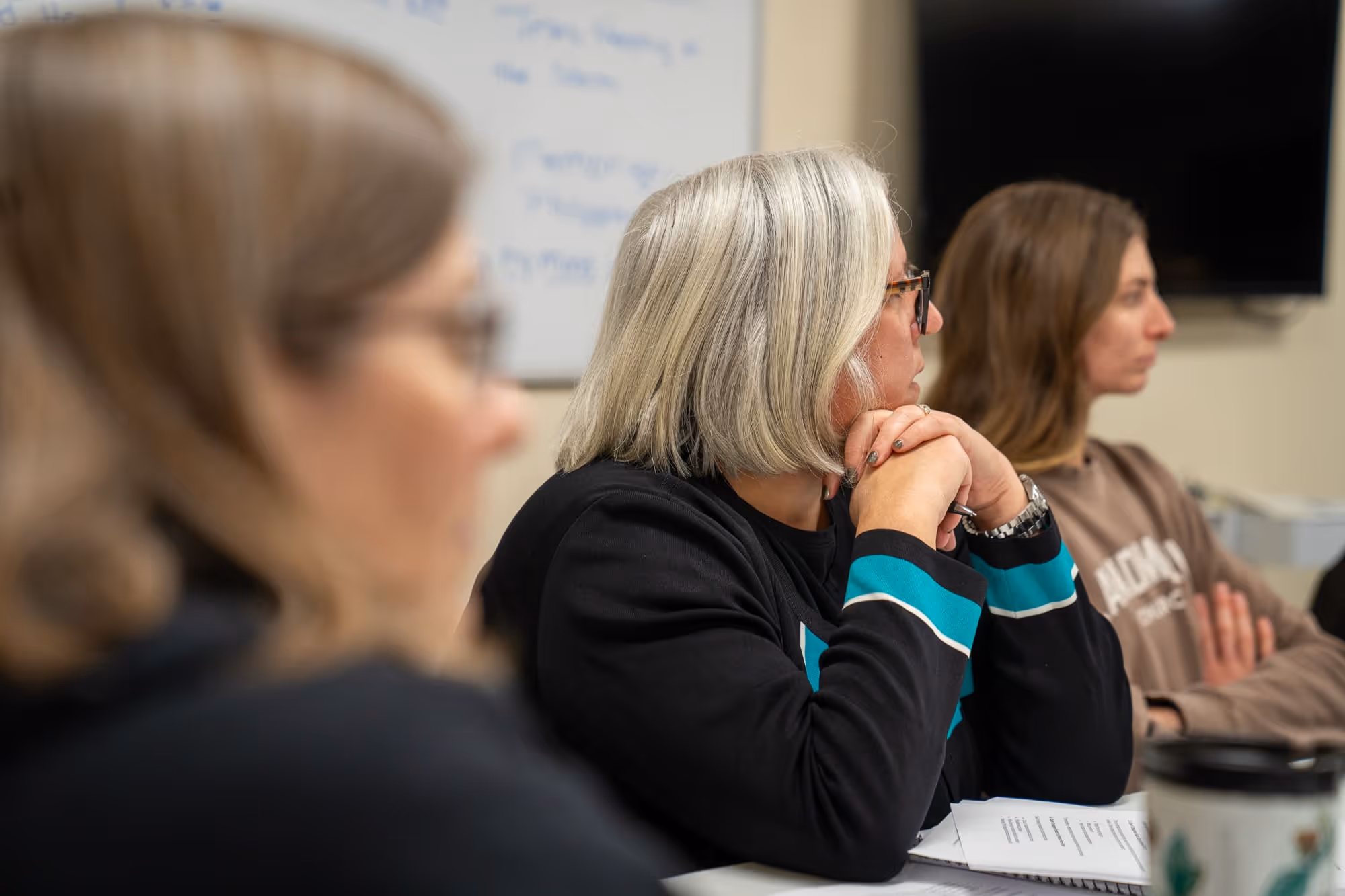 Women sitting in meeting at church or hospital, engaged and attentive with papers and whiteboard.