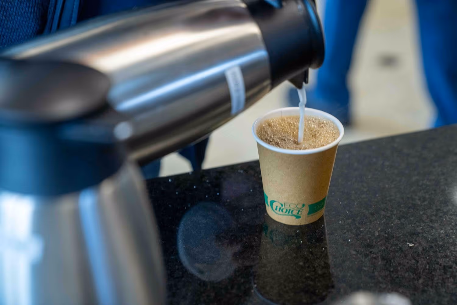 Coffee pouring into a paper cup on a black counter in hospital or church setting.